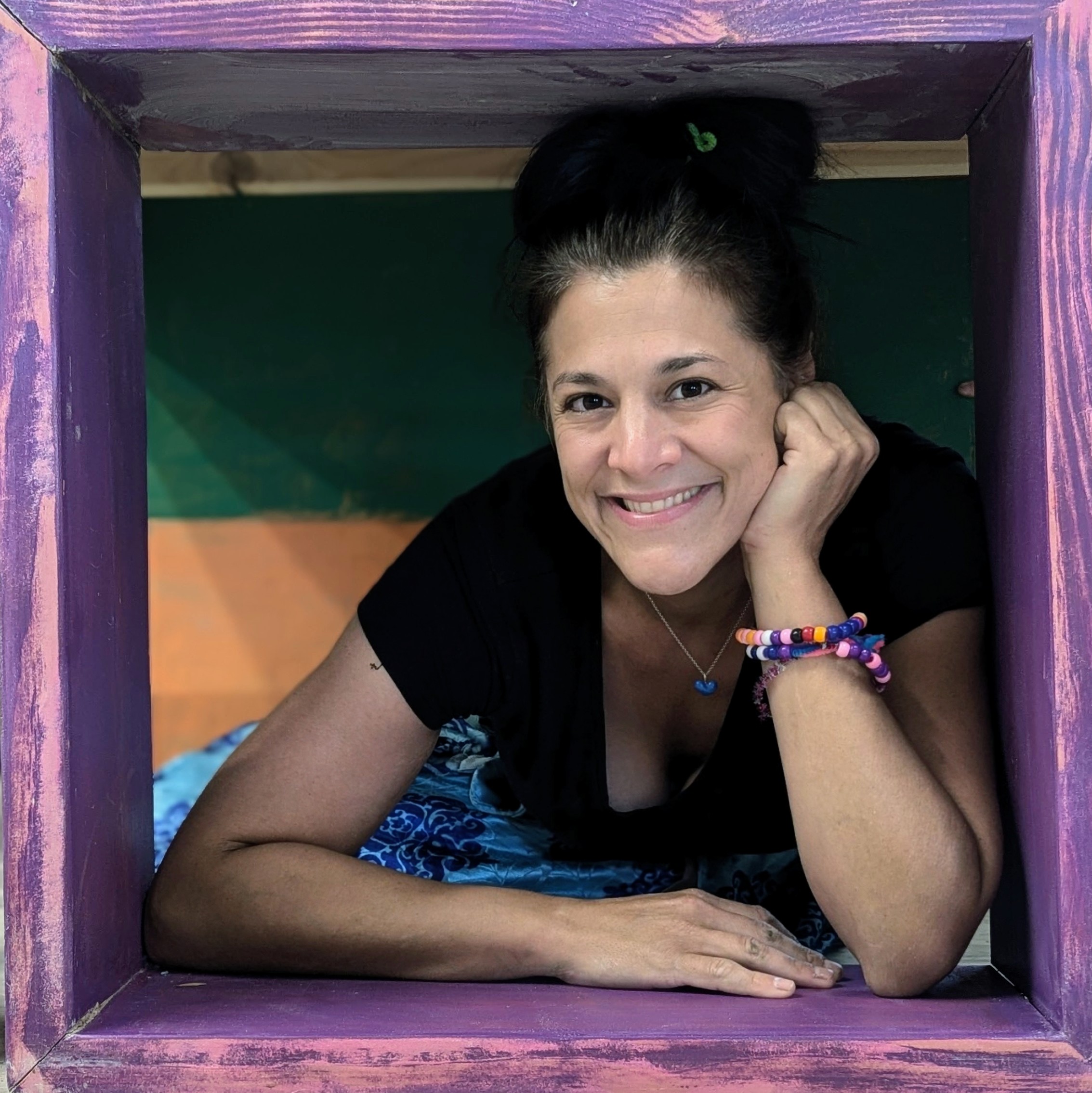 Woman smiling, resting her head on her hand, framed by a purple square, background with green and orange colors.