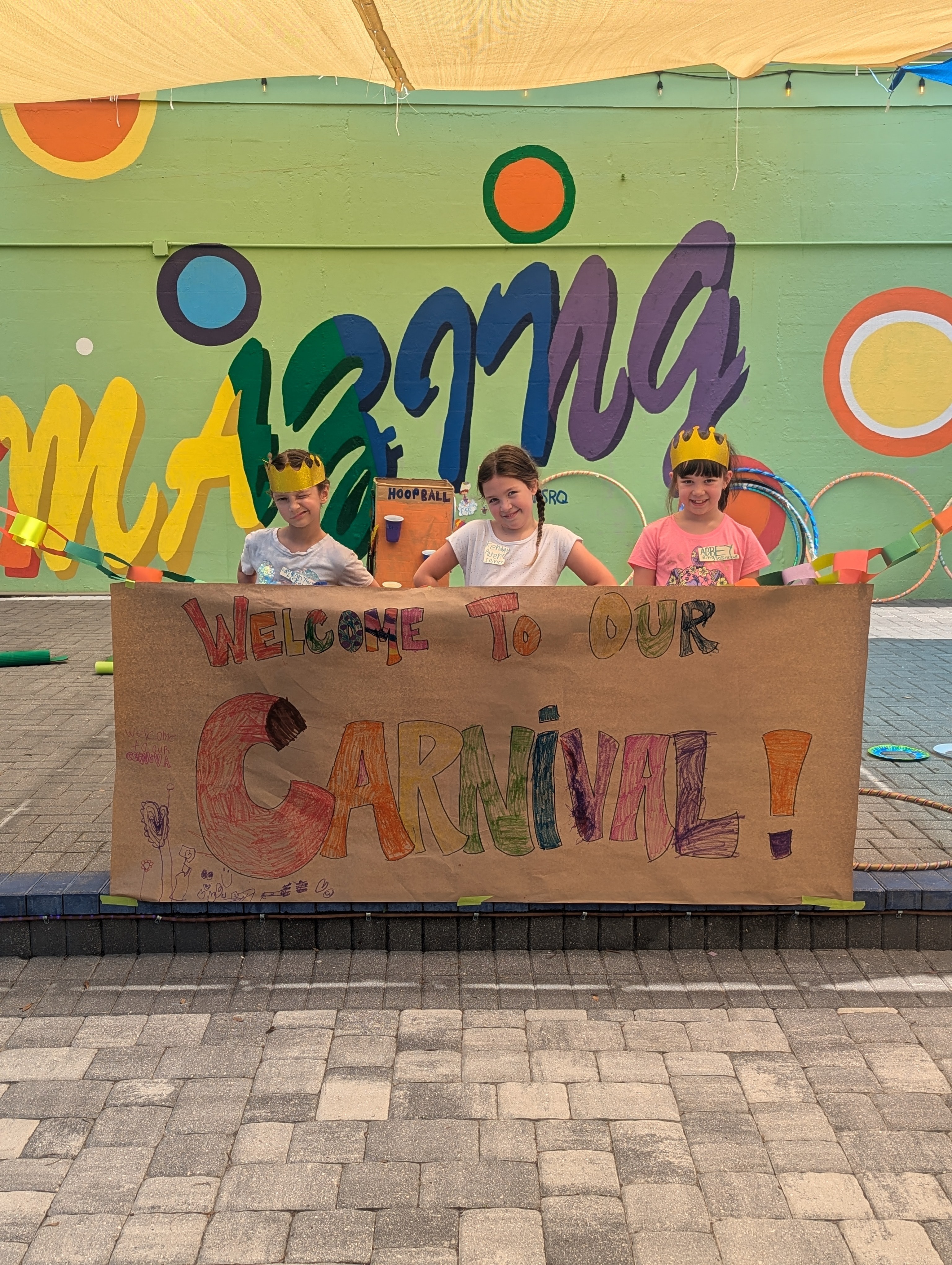 Three children holding a colorful banner on a stage with a vibrant background and the word 'summer' in large letters.
