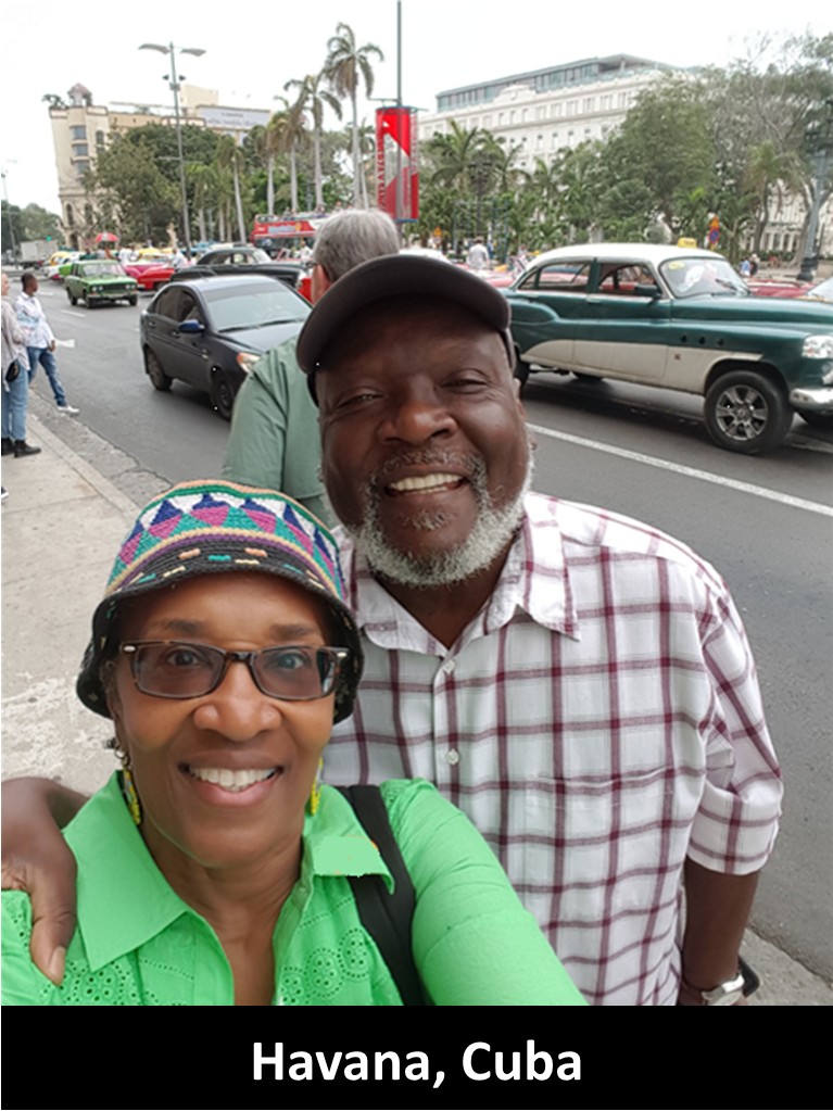 Two smiling people taking a selfie on a busy street in Havana, Cuba, with cars and buildings in the background.