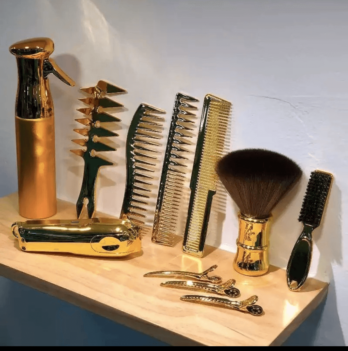 Collection of gold and black grooming tools including spray bottle, razors, combs, brush, and scissors on a wooden surface.