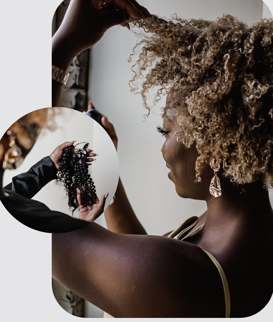 Woman with curly hair getting a hair treatment, holding a section of hair, with a stylist in the background.