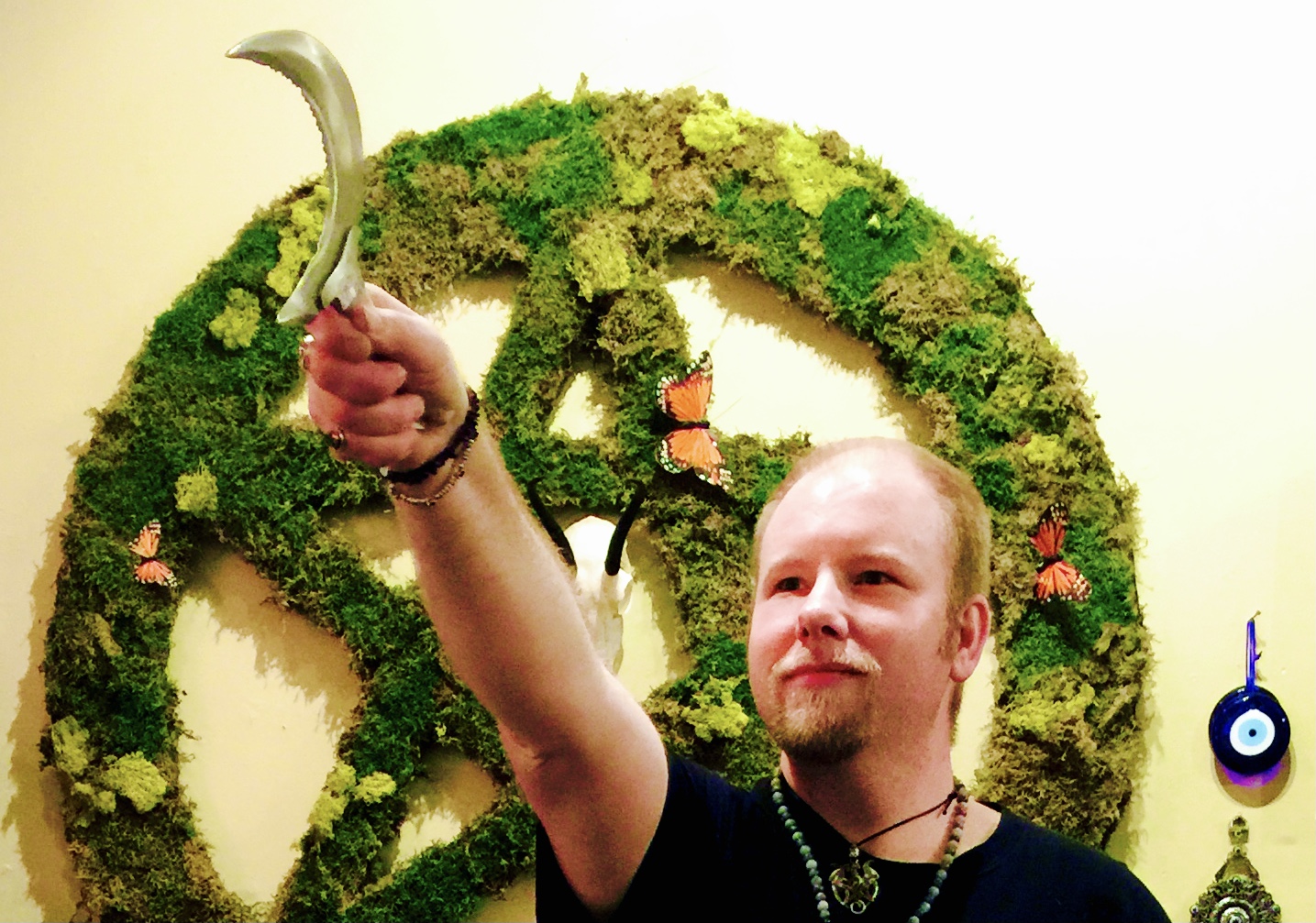 Person holding a curved object in front of a large green moss wall with butterflies and a hanging decoration.