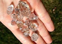 Hand holding several large, clear, irregularly shaped crystals outdoors with grass in the background.