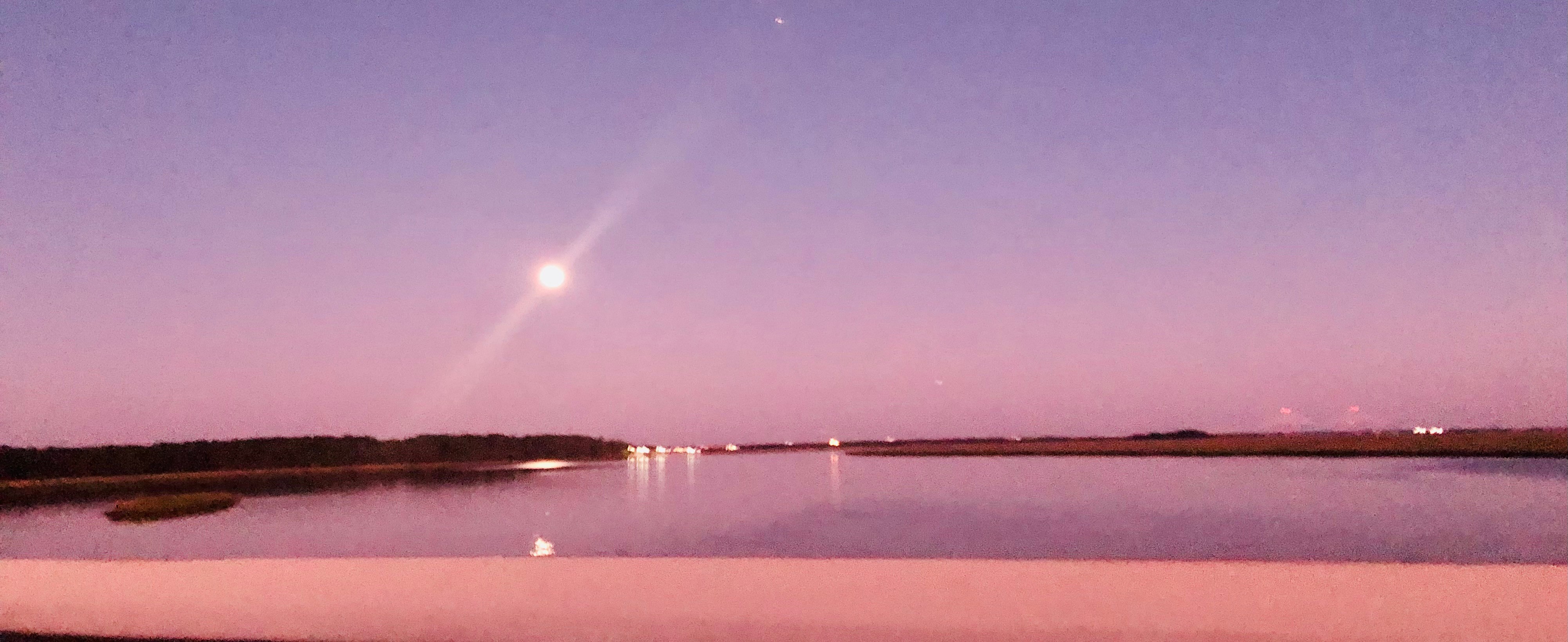 Sky with a bright streak of light, reflected on calm water, with a horizon line and pinkish-purple hues.