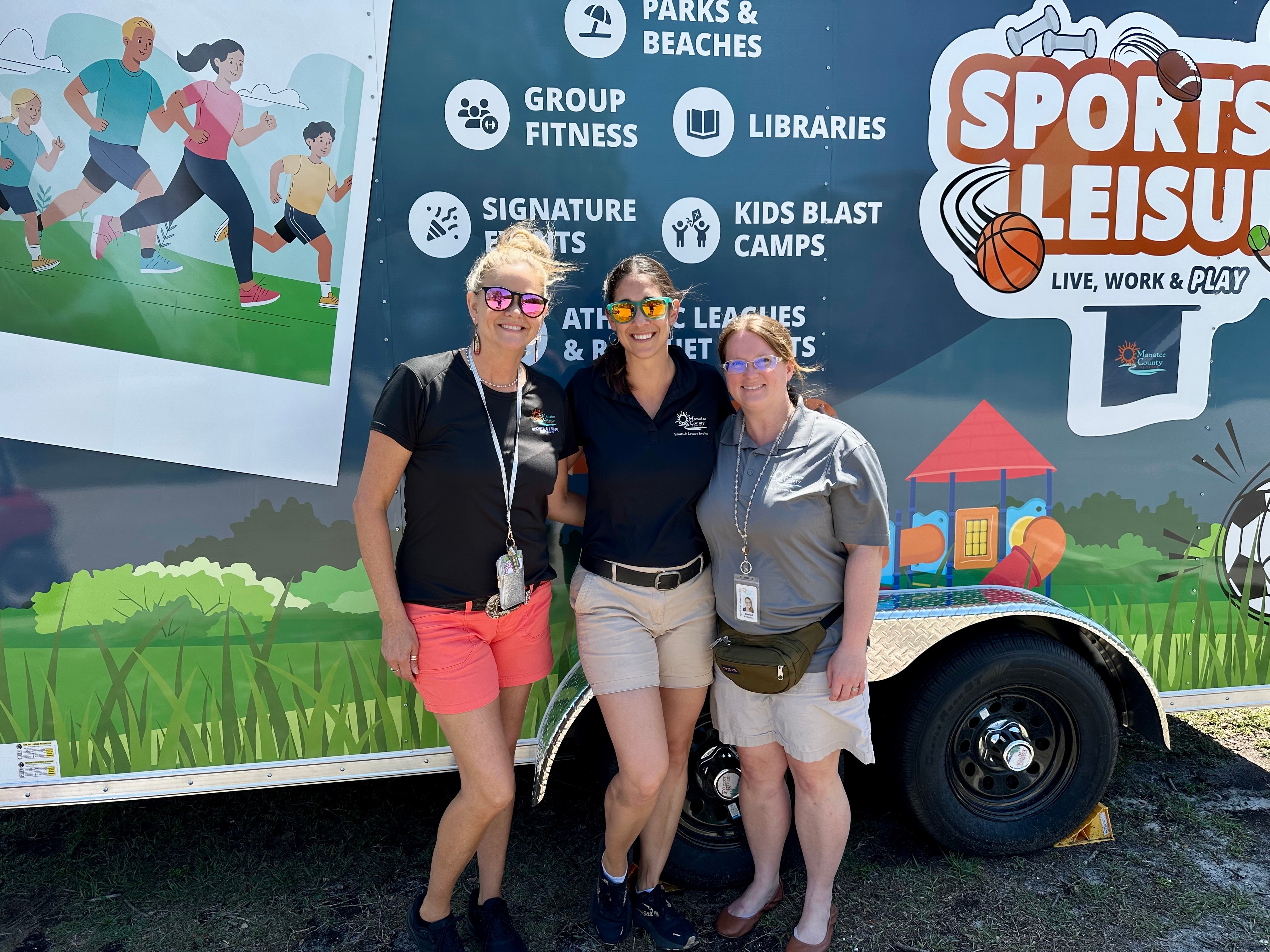 Three women standing together in front of a colorful sports and leisure vehicle, smiling outdoors.