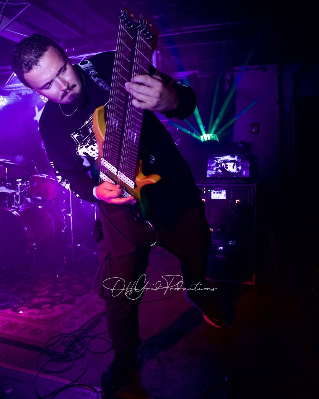 Person playing an electric guitar on stage with colorful lights in the background.
