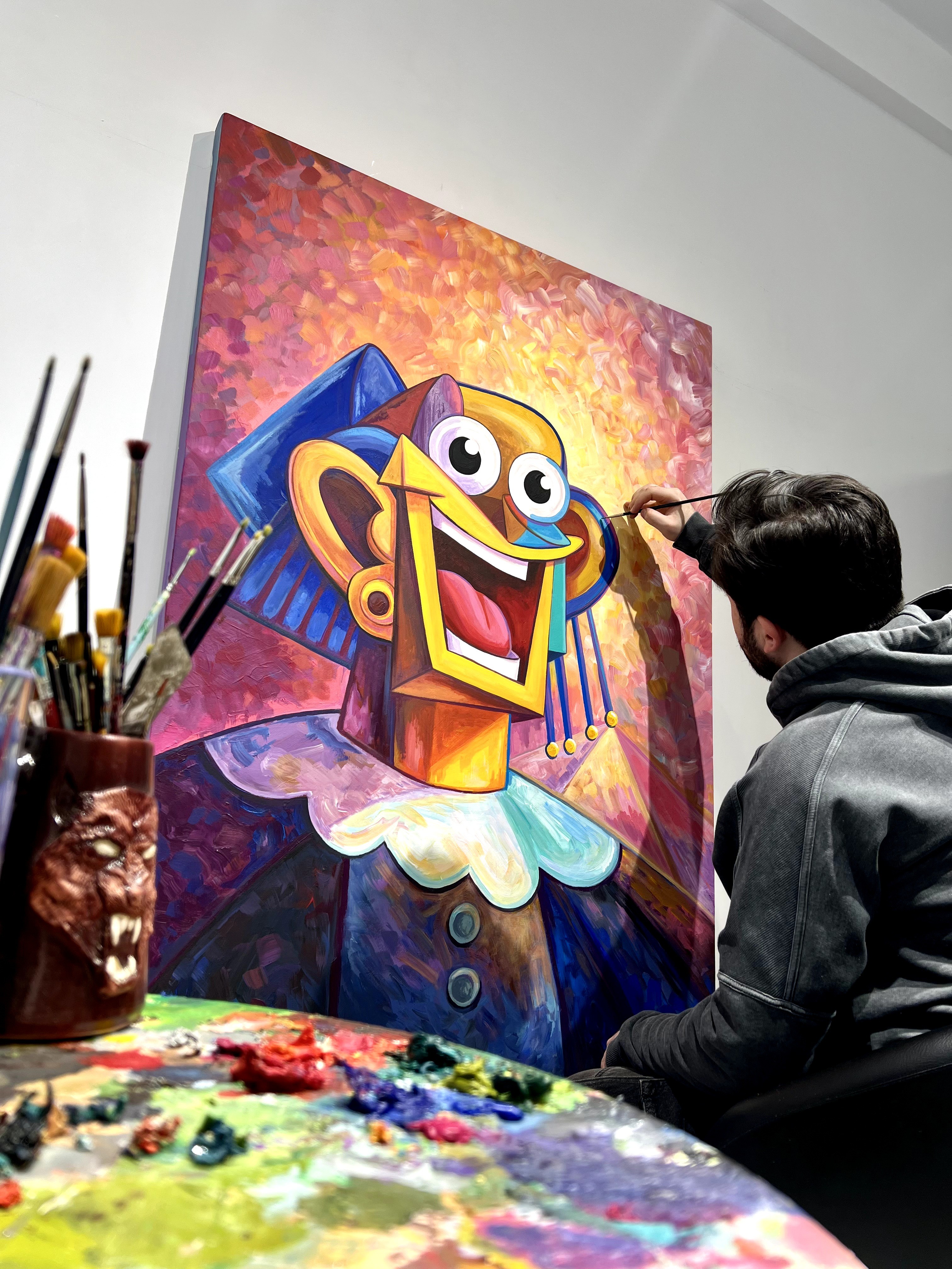 Artist working on a colorful, cartoonish painting of a character with large eyes, a wide smile, and vibrant colors.