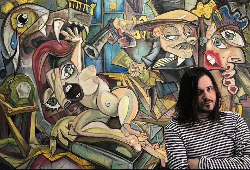 Person with long dark hair and striped shirt standing in front of colorful abstract mural with various faces and figures.