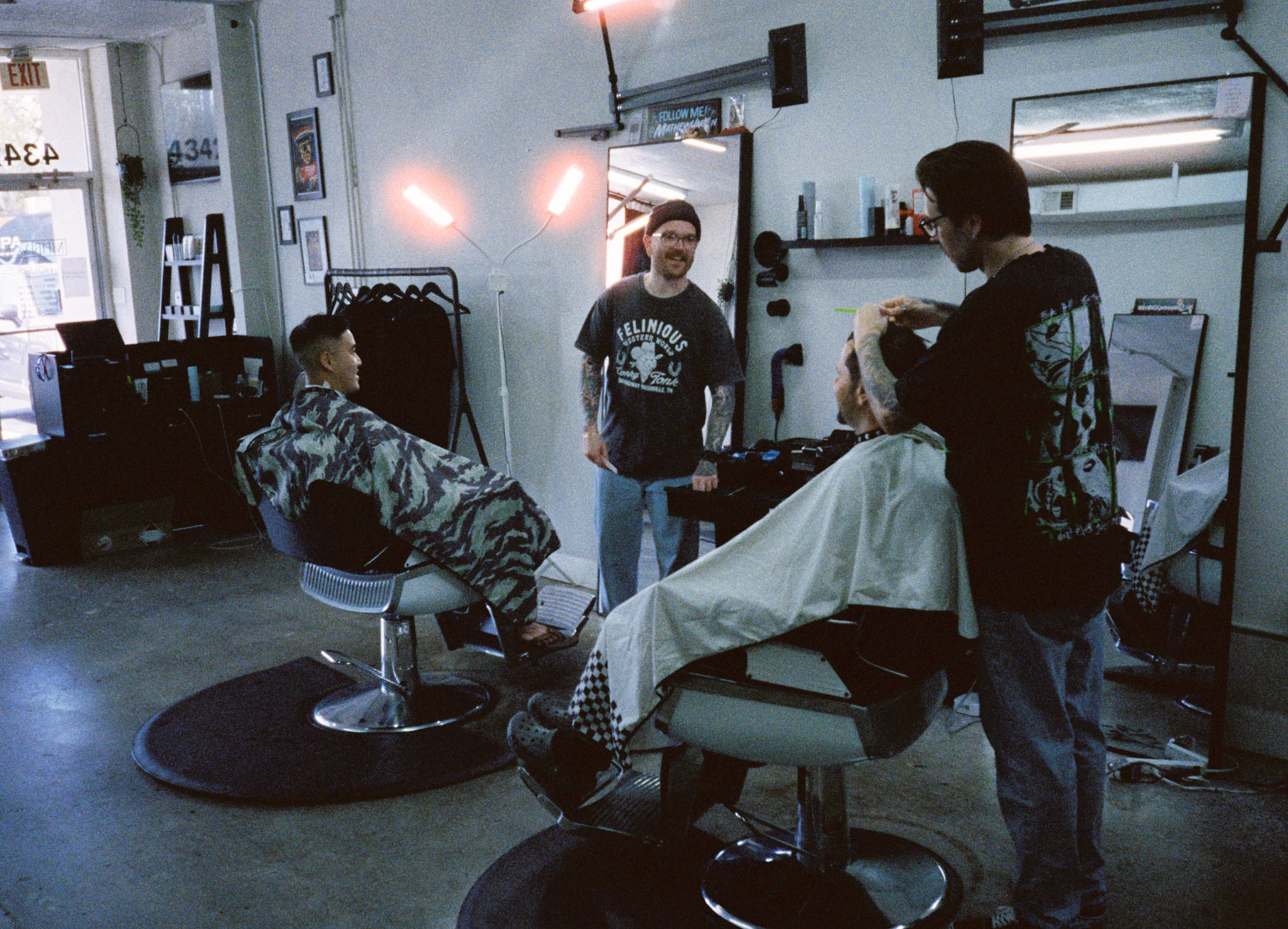 Barber shop with two barbers working on clients, mirrors, and salon equipment visible, interior with bright lighting.
