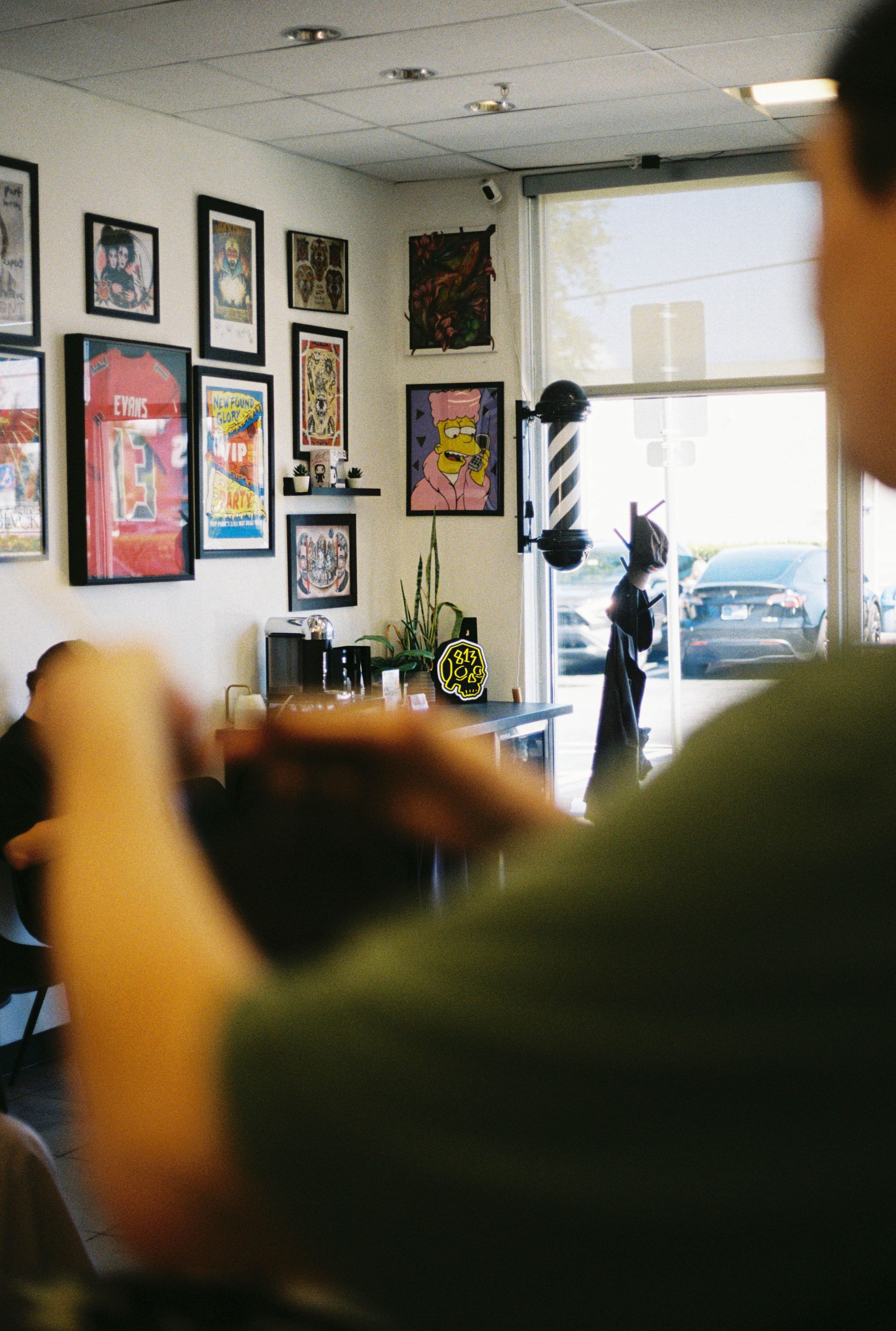 Person in green shirt using a smartphone inside a room with framed artwork on the wall and a large window.