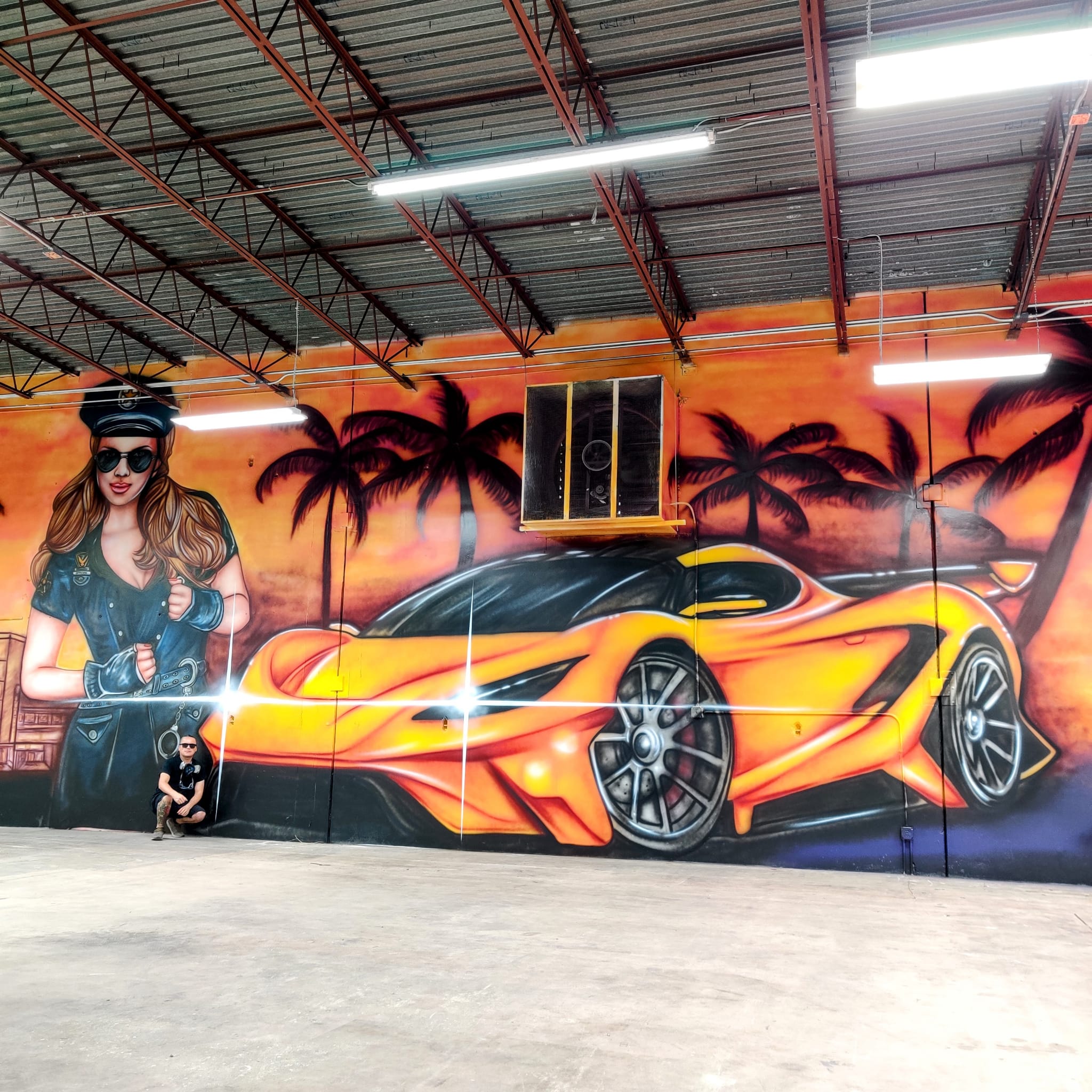 Colorful mural of a woman with sunglasses and a sports car with a sunset background, palm trees, and a small dog.