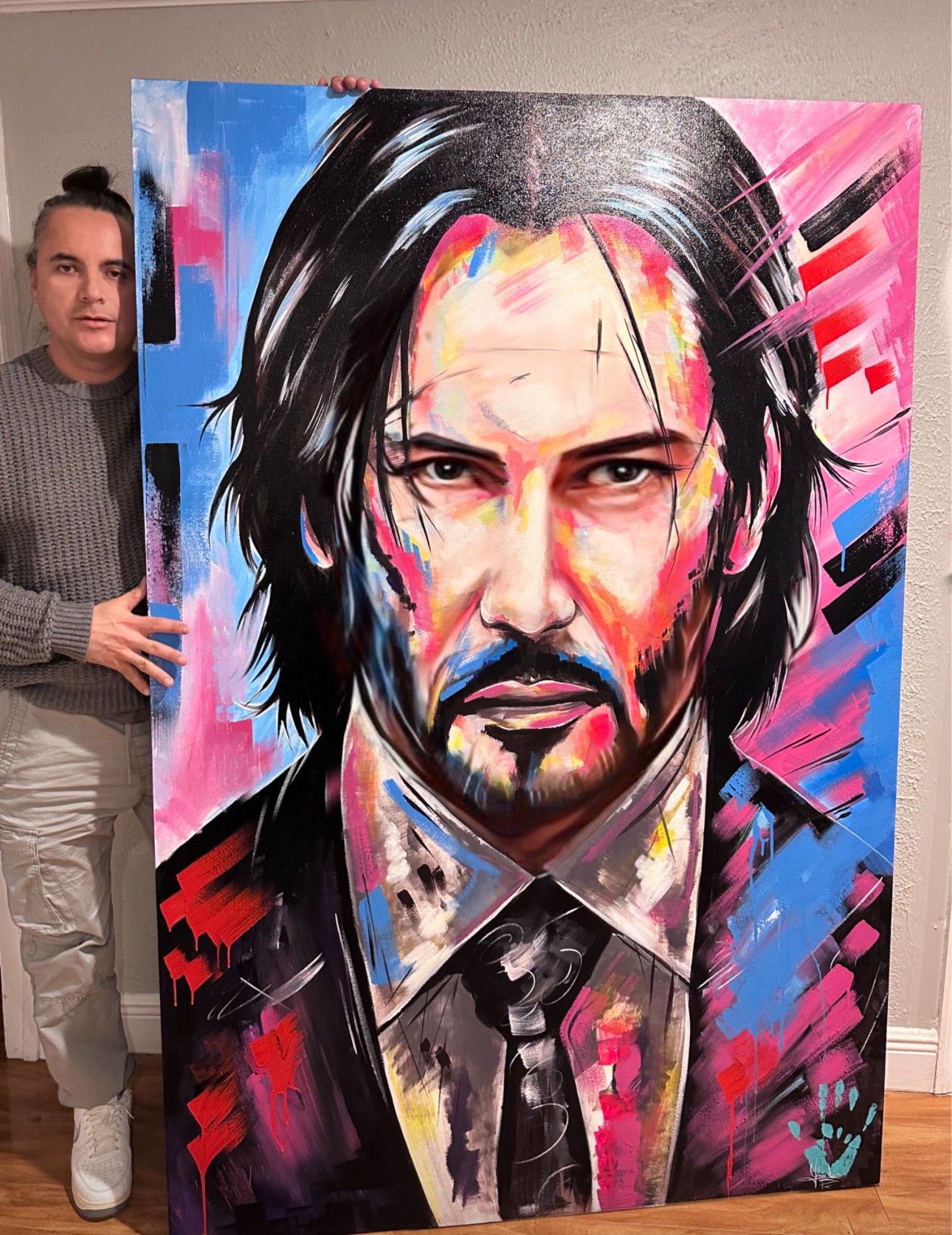 Person holding a colorful portrait of a man with long dark hair, beard, and intense expression, painted in an abstract style.