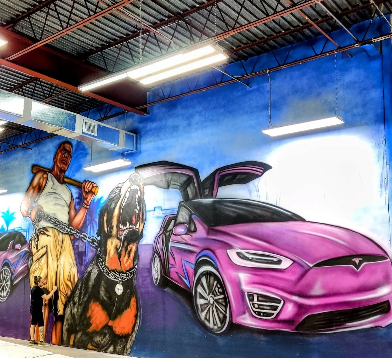 Indoor mural featuring a woman, a large dog, and a pink Tesla car with open doors, painted on a blue wall.