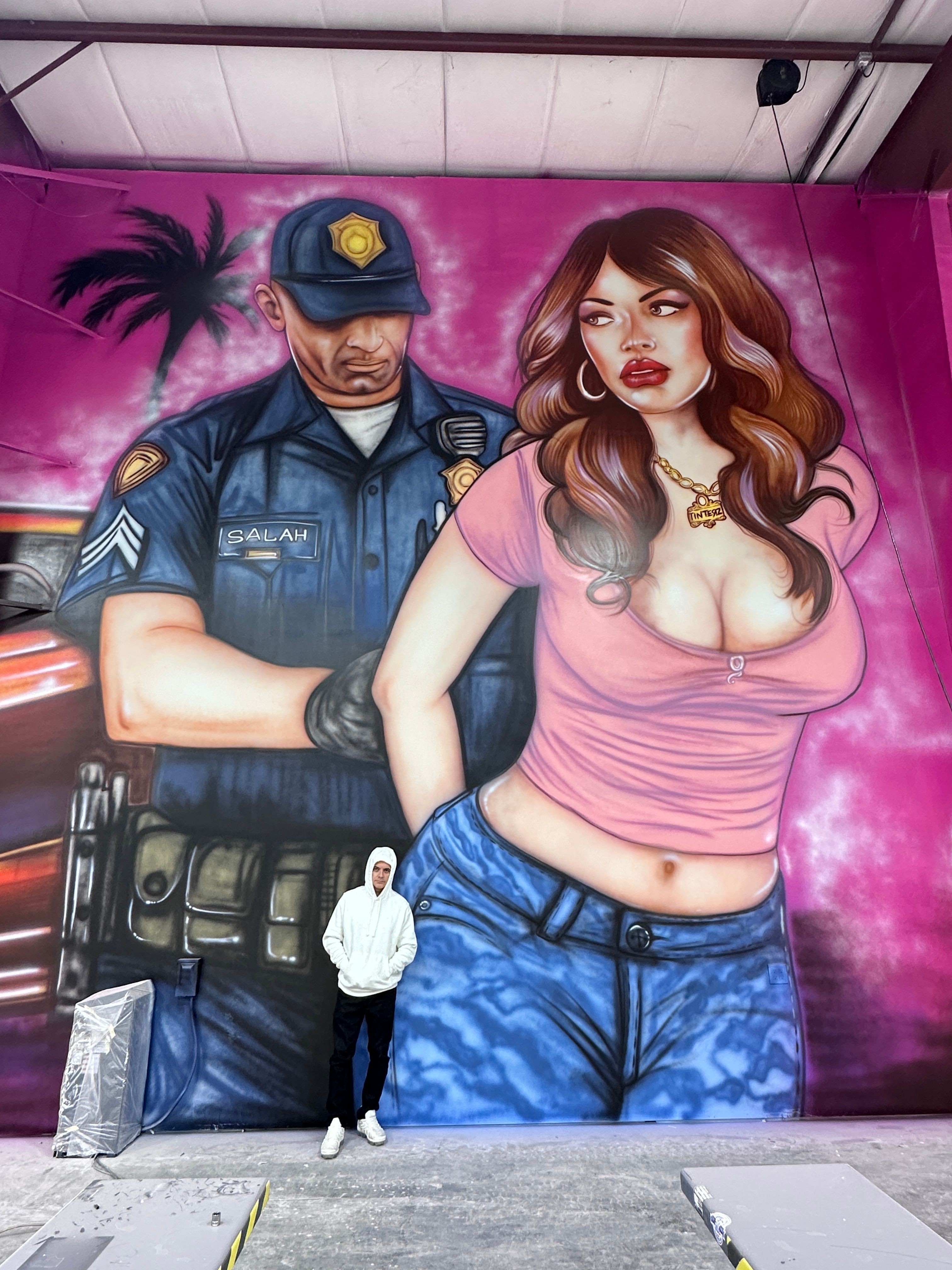 Mural of a woman in pink top and jeans, and a police officer in uniform, standing together against a pink background.