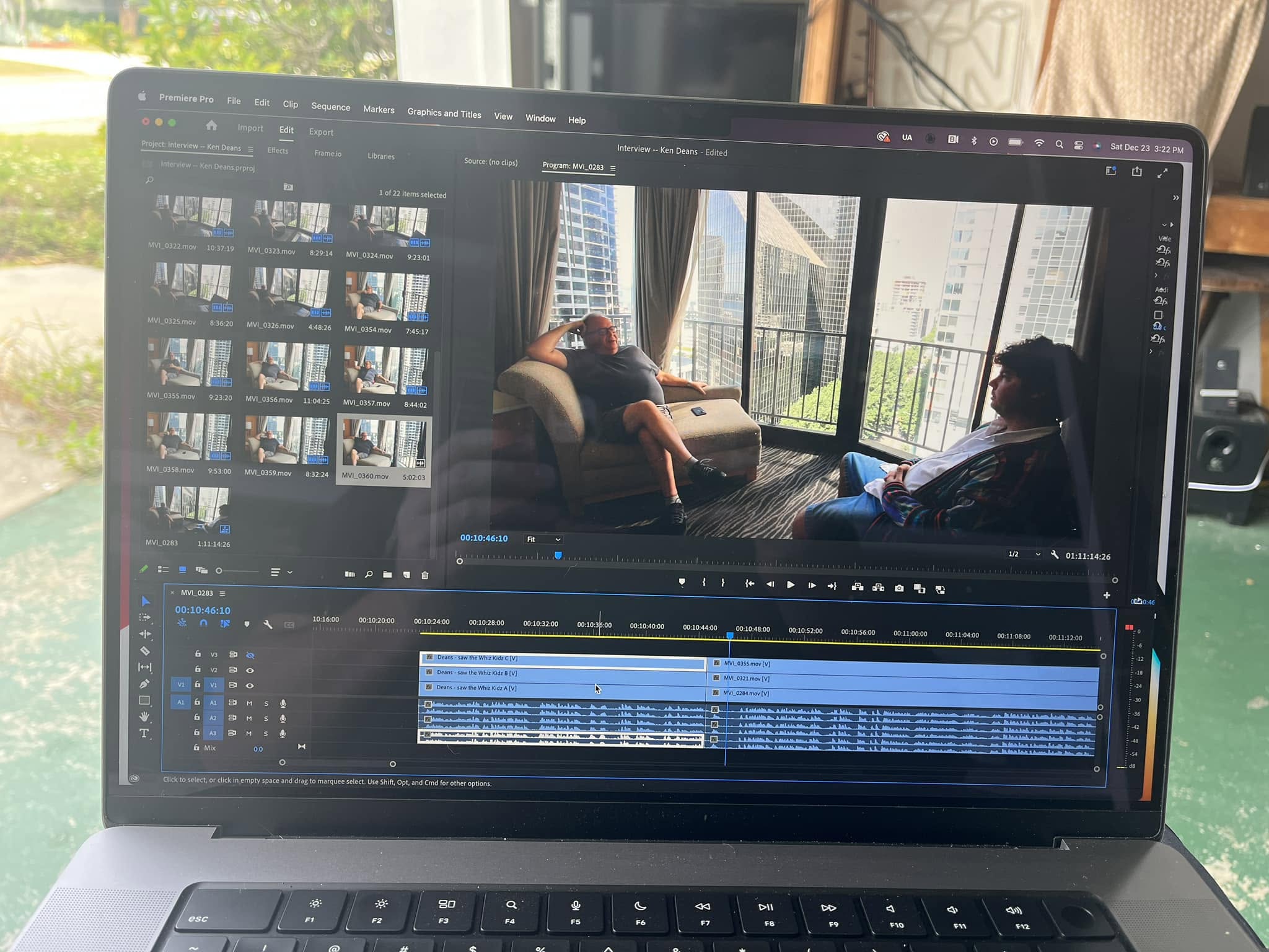 Laptop screen displaying video editing software with a scene of two people sitting in a room with large windows and city view