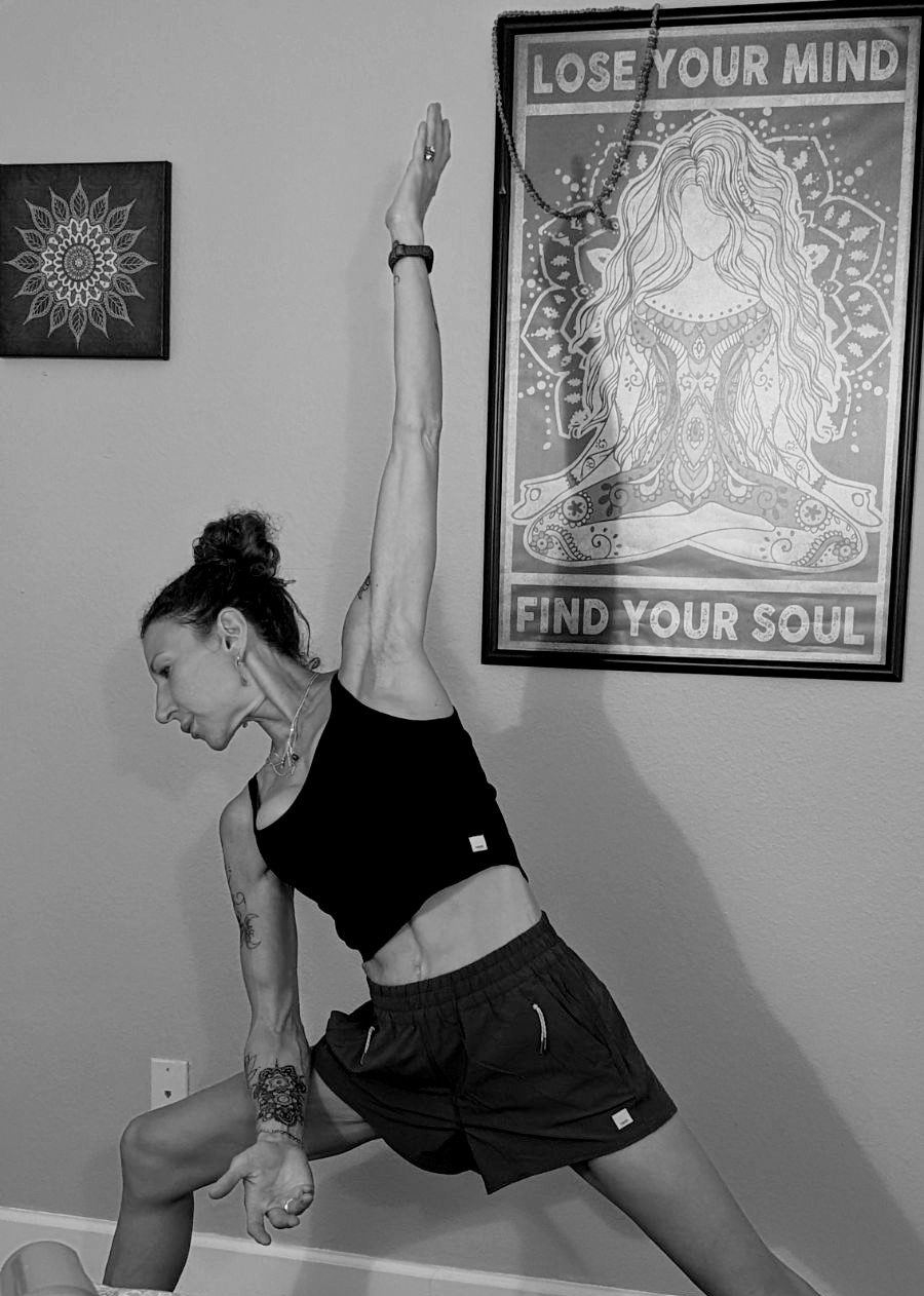 Woman stretching in a room with framed artwork on the wall, one with a mandala and another with a woman and text.
