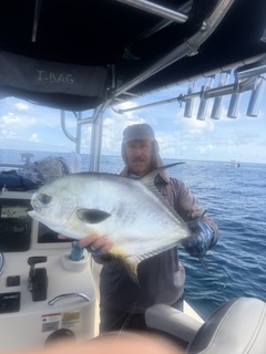 Person holding a large fish on a boat with ocean and sky in background.
