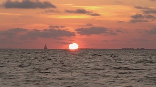 Sunset over the ocean with a sailboat on the horizon, orange and pink sky, calm water