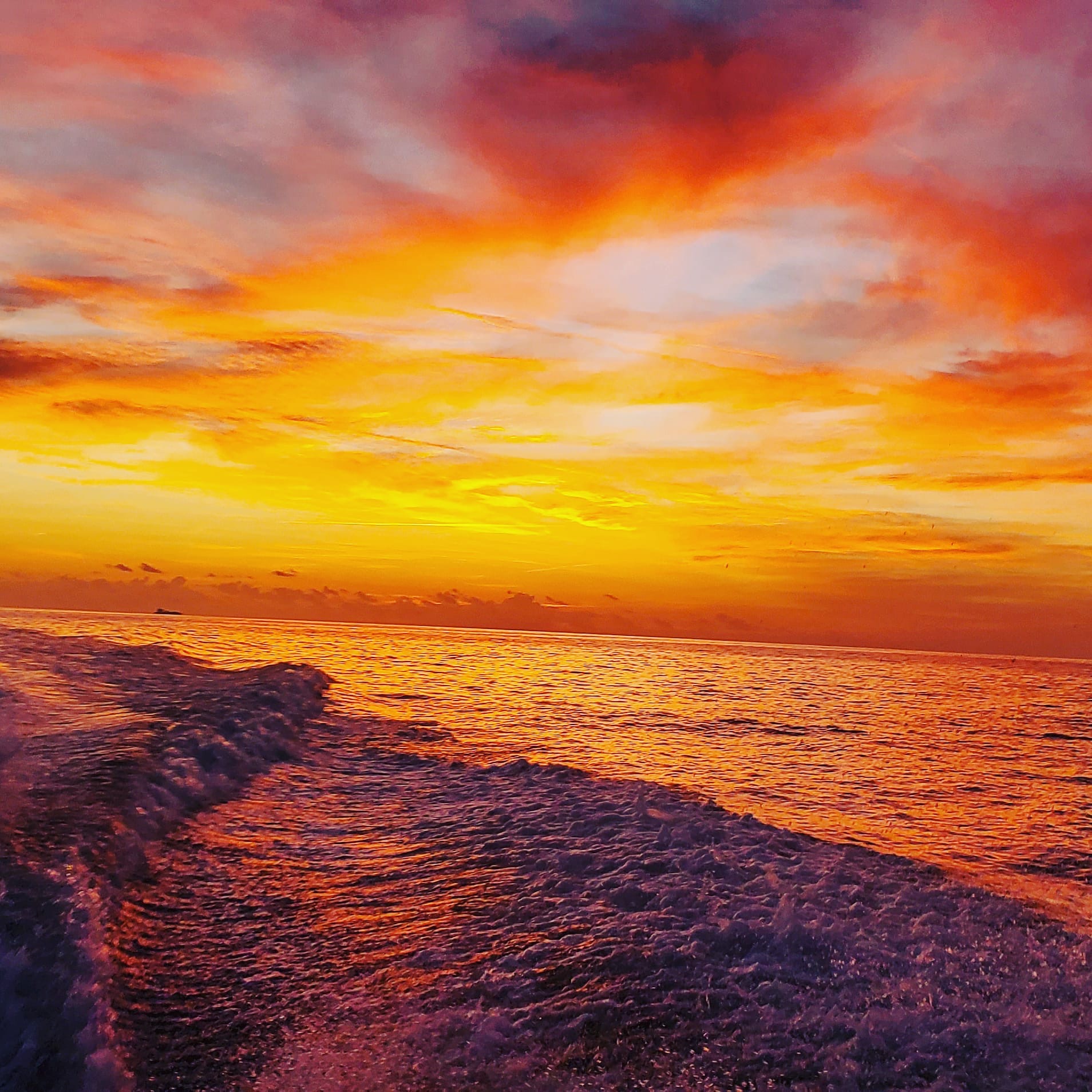 Sunset over the ocean with colorful sky and waves crashing on rocks.