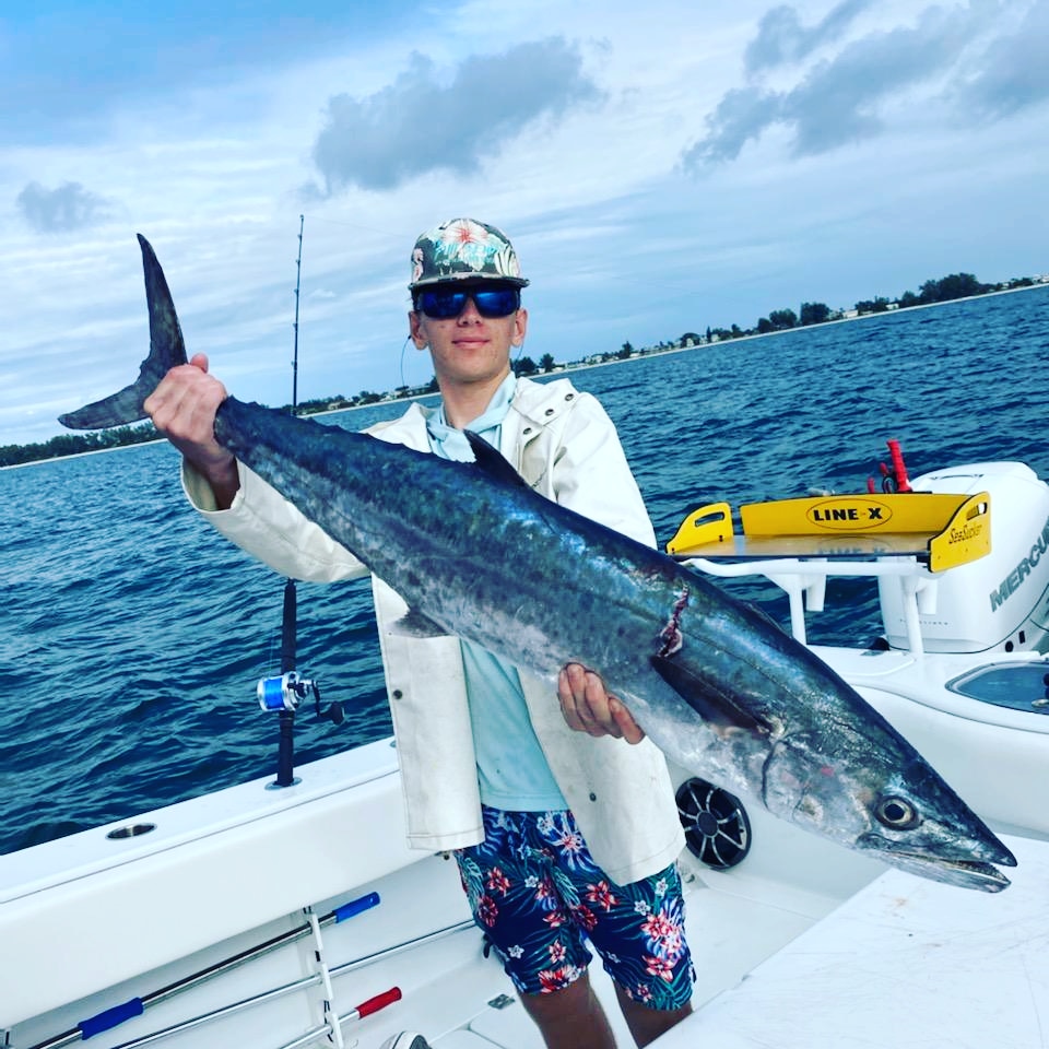 Person holding a large fish on a boat with water and sky in background.