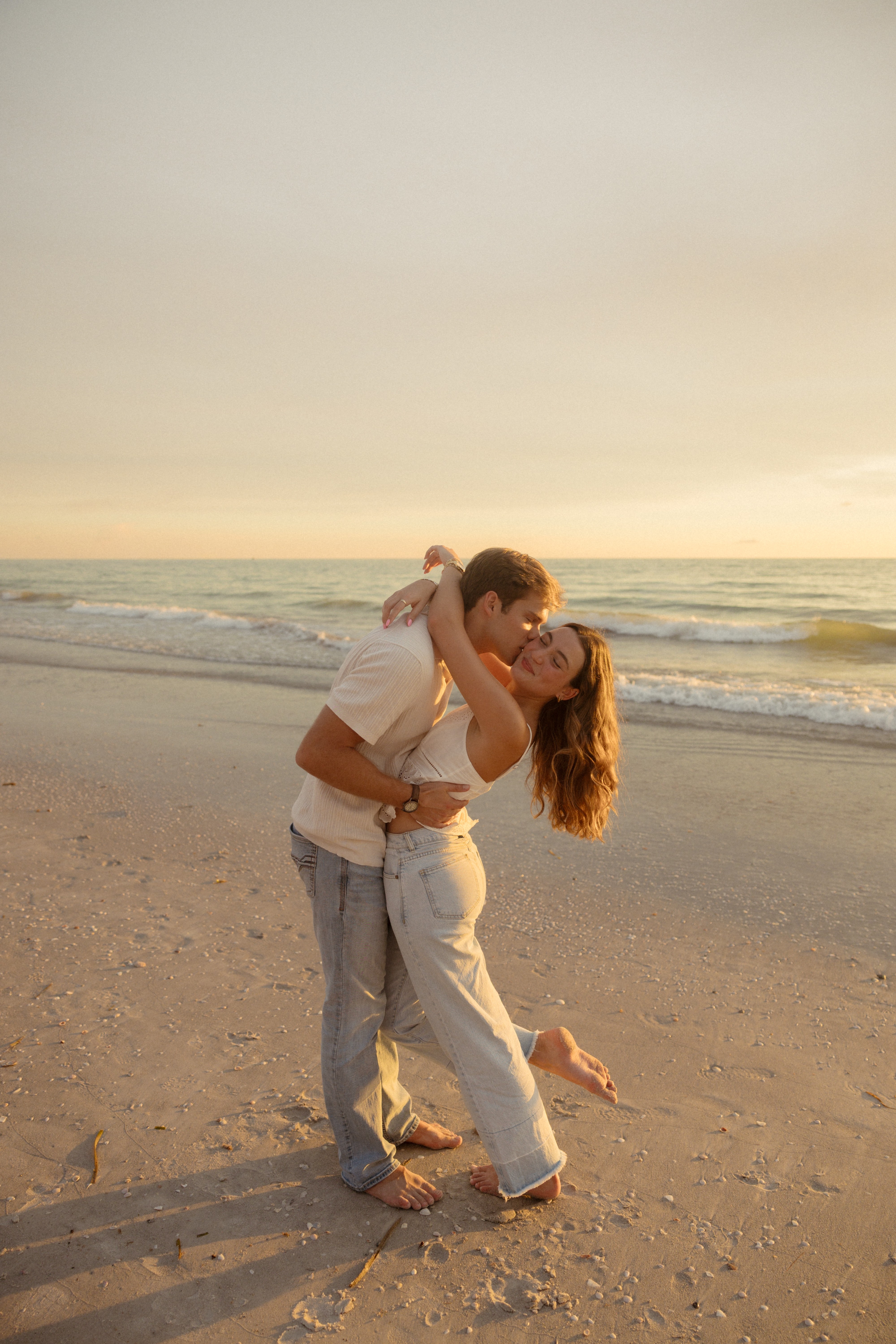 A couple dancing on the beach at sunset, with the ocean and sky in the background.
