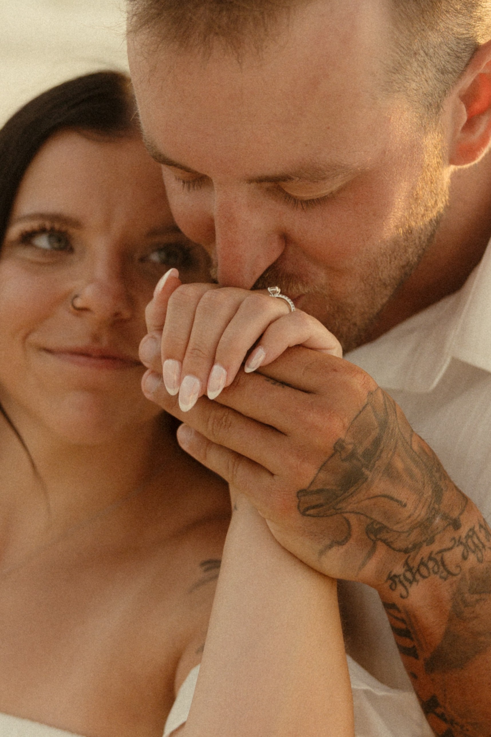 A man kisses a woman's hand, both with light skin, in a close-up shot.
