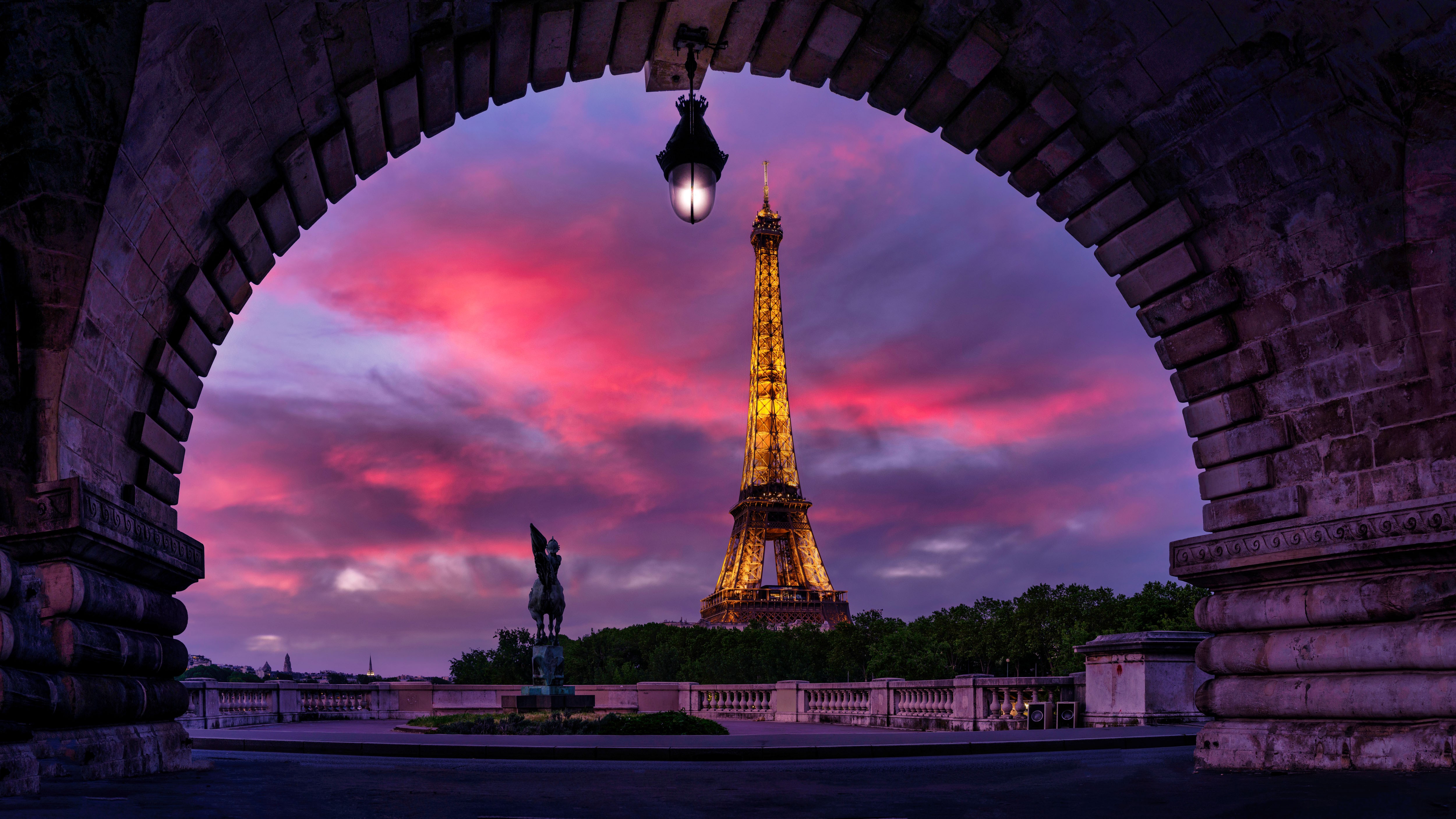Eiffel Tower viewed through an archway with a colorful sunset sky in the background.