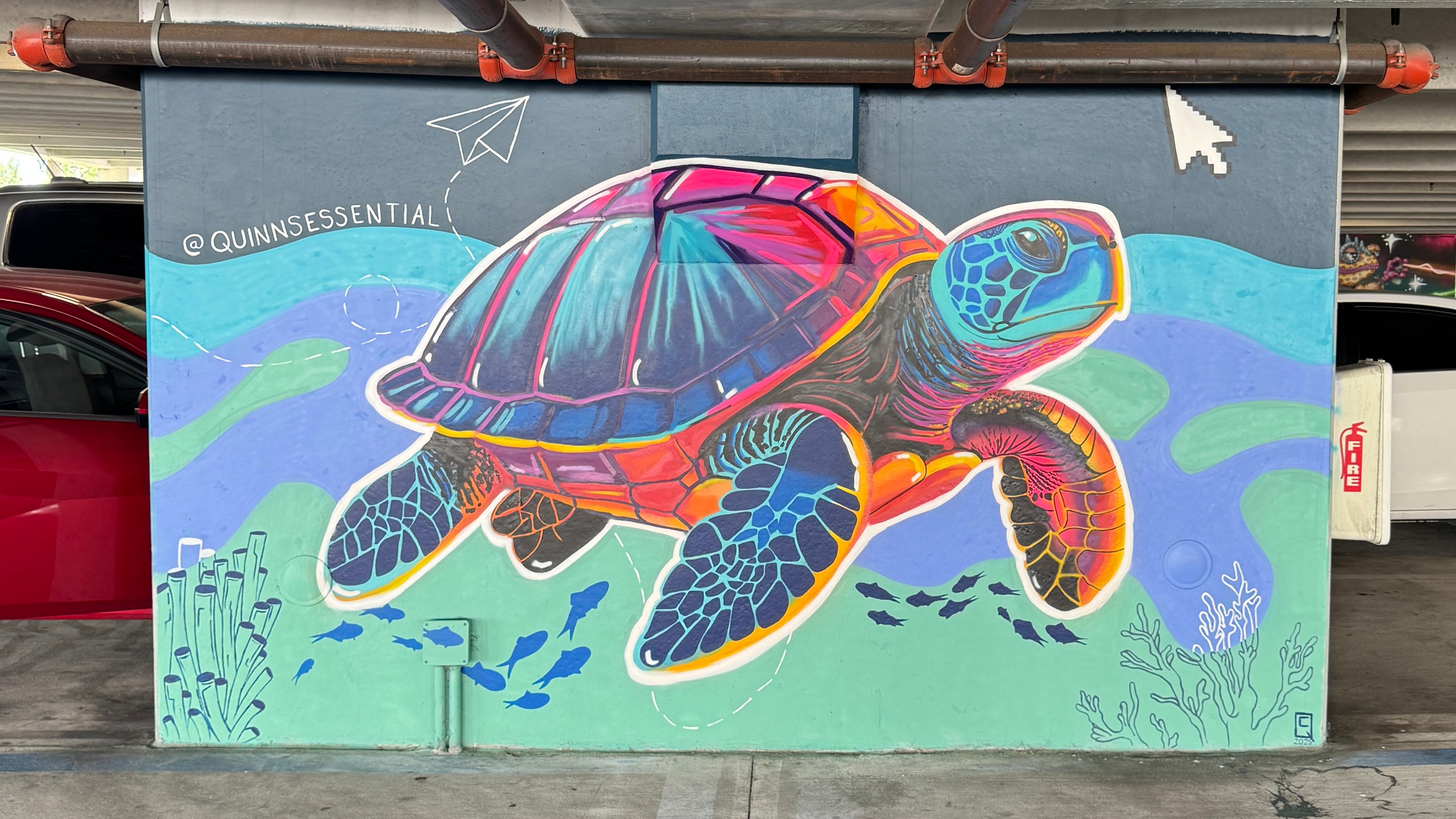 Colorful turtle mural with vibrant patterns swimming underwater, surrounded by aquatic plants and fish, on a wall.