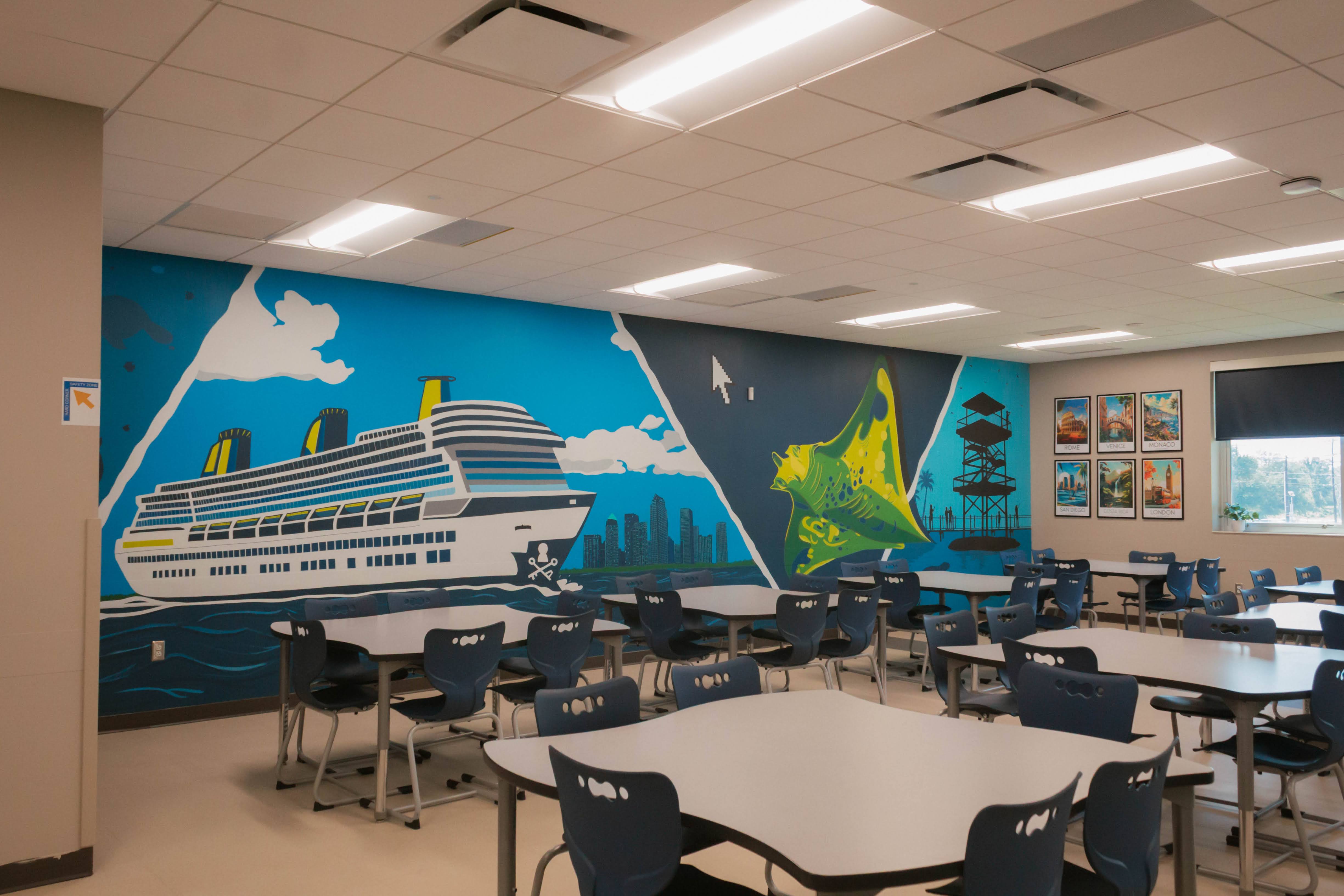 Classroom with a large mural of a cruise ship, a green sailboat, and a pagoda, with tables and chairs arranged for students.
