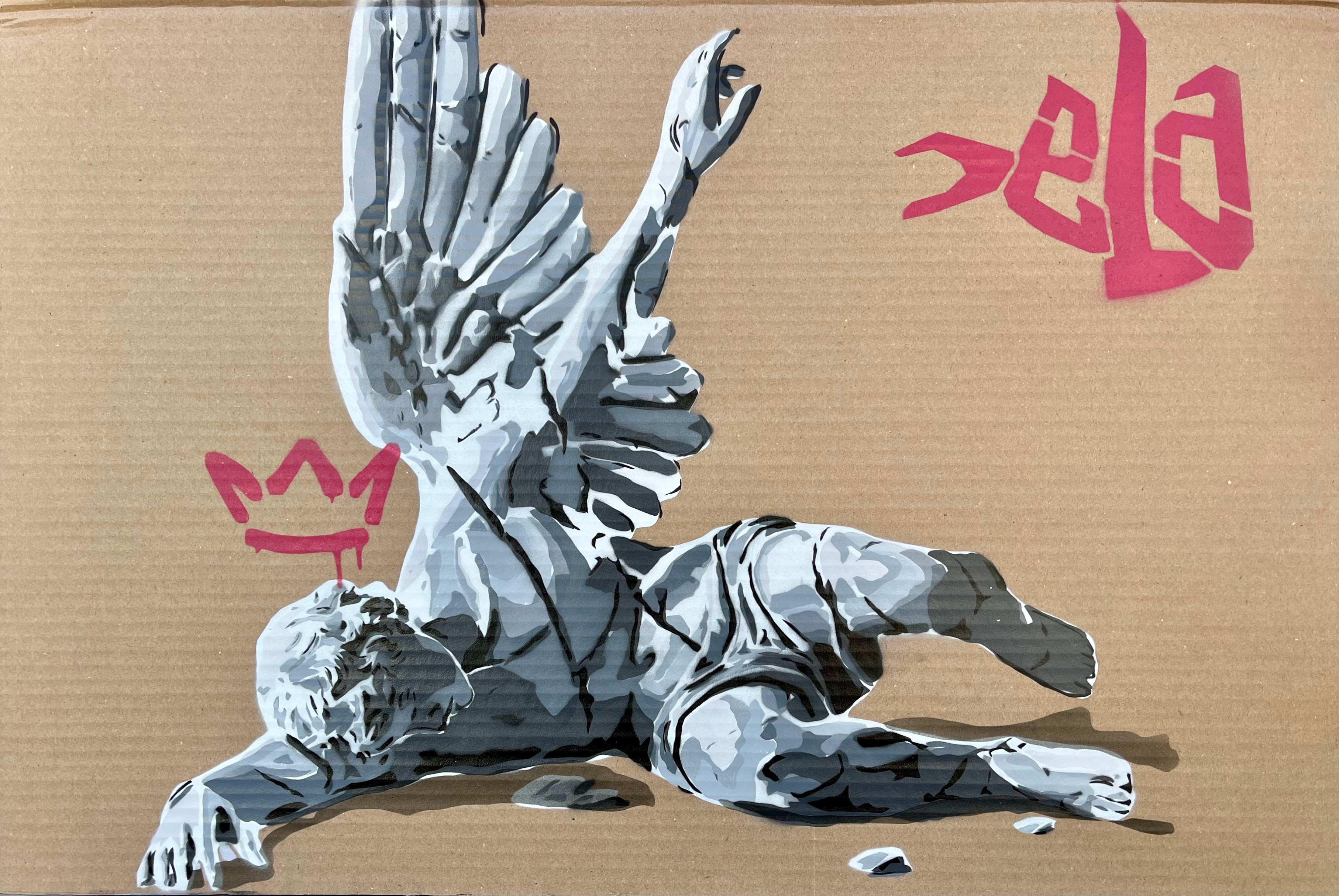 Street art of a metallic sculpture of a person lying down with one hand raised, on a cardboard background with pink graffiti.
