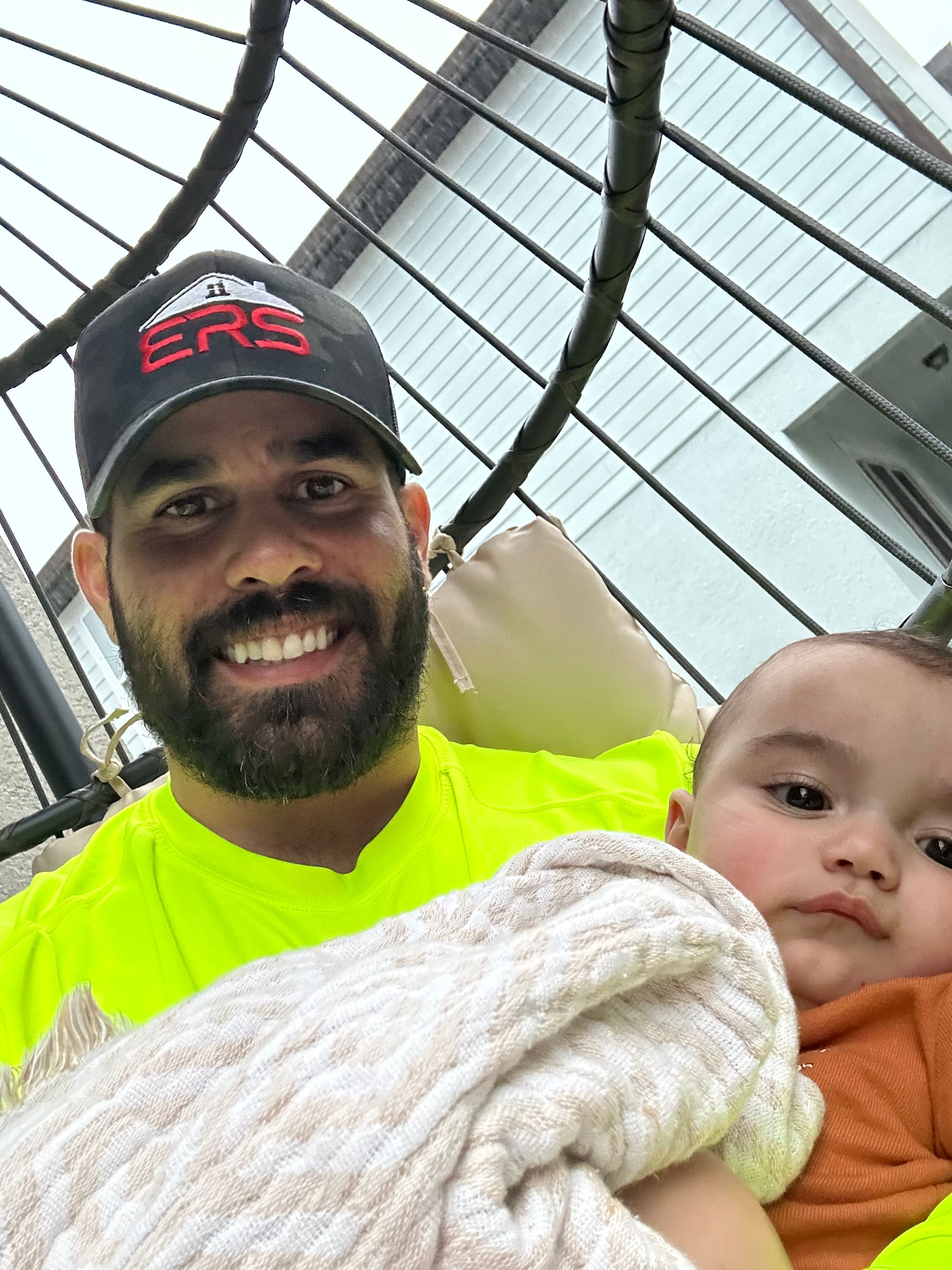 Man with a beard and cap lying with two children, one child looking at the camera, in a cage-like structure.