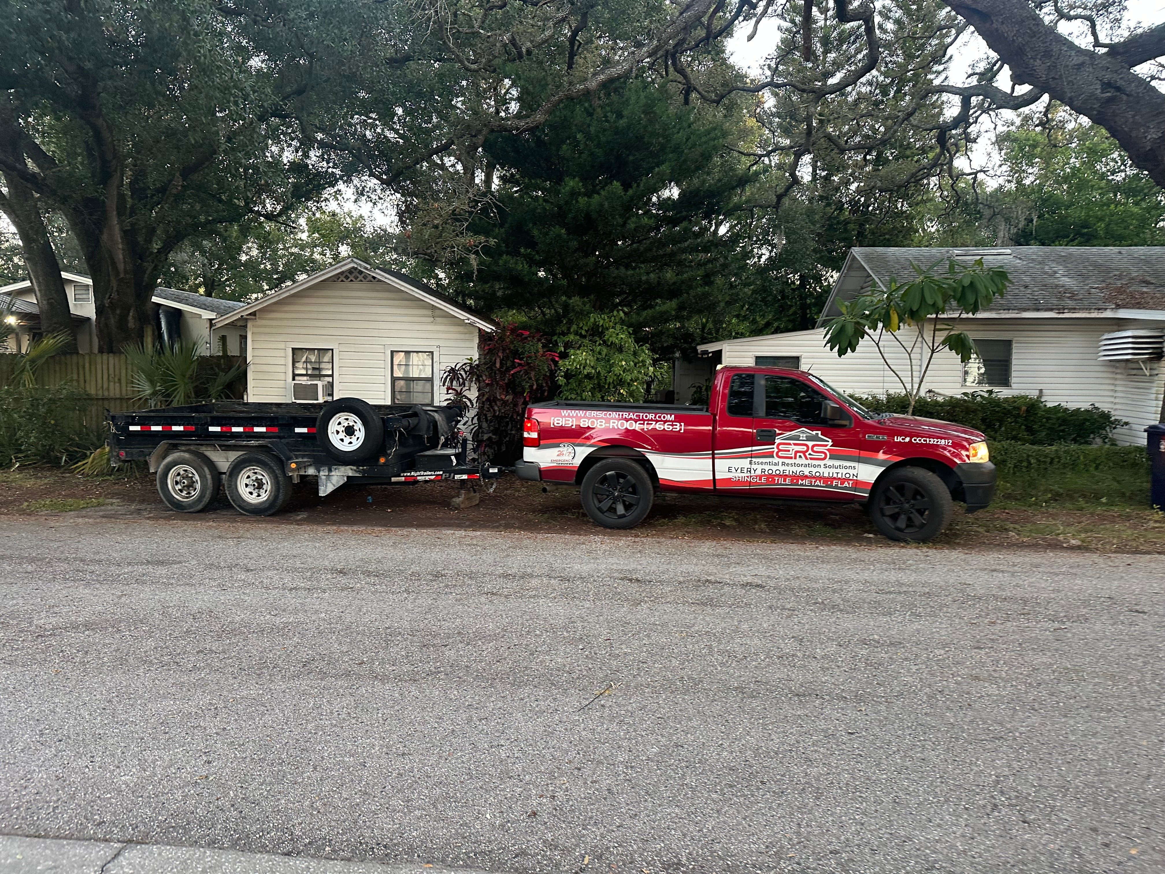 Red pickup truck with a trailer attached parked on a residential street, trees and houses in the background.