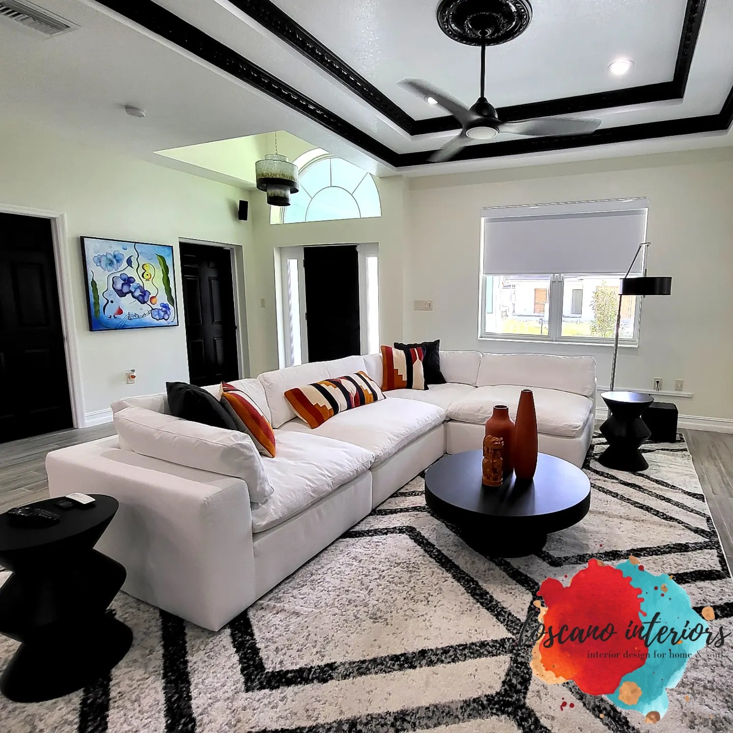 Living room with white sectional sofa, black round coffee table, and decorative vases, featuring a ceiling fan and artwork on the wall.