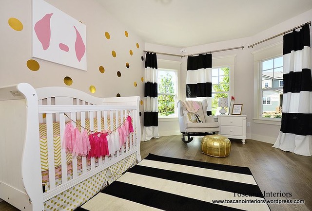 Nursery room with white crib decorated with pink tassels, black and white curtains, a white desk, and a gold pouf.