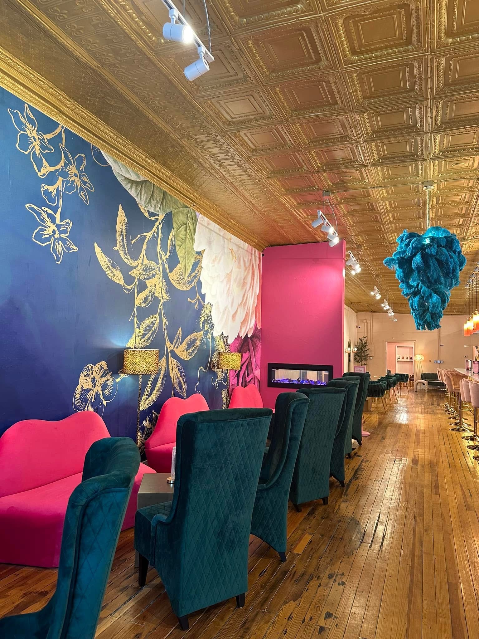 Interior with colorful walls, velvet chairs, and decorative ceiling, featuring a large blue floral mural and hanging blue art piece.