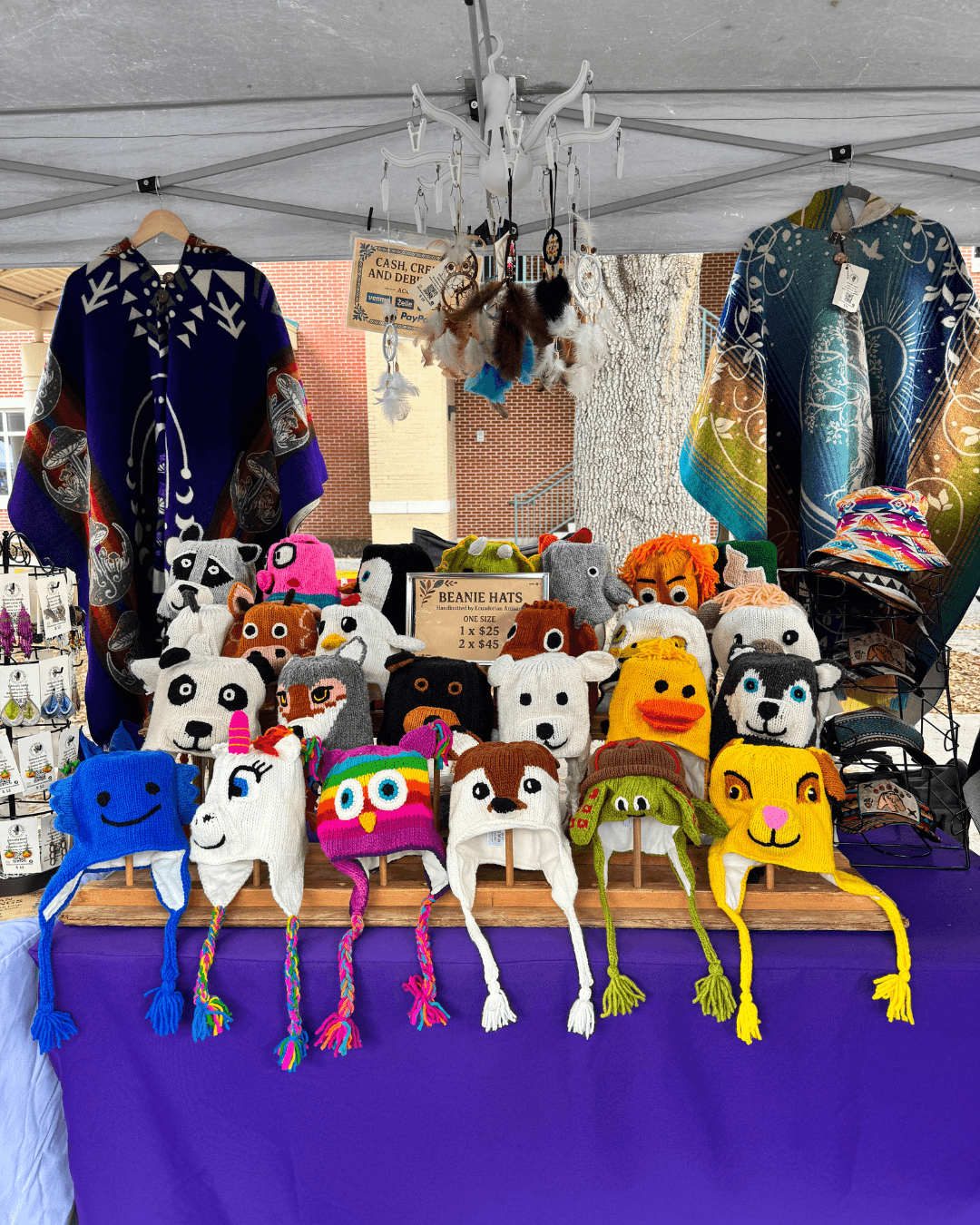 Display of colorful handmade hats and plush toys at a market stall with clothing in the background.