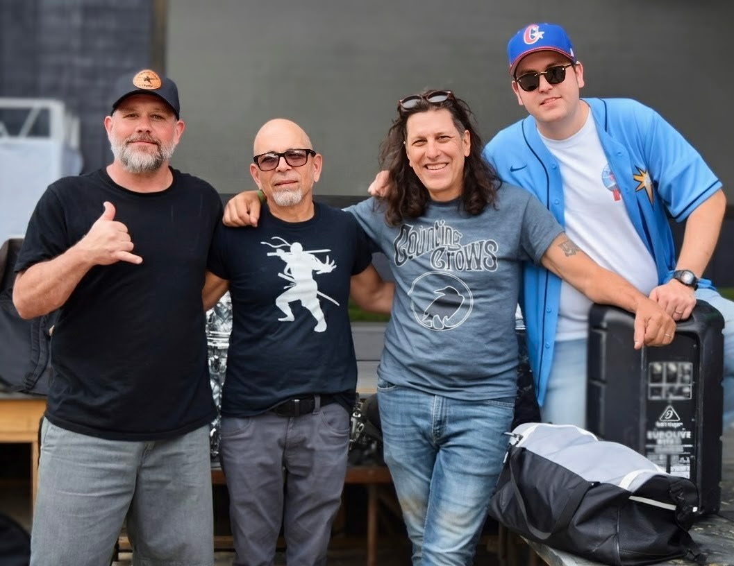Four people standing together outdoors, smiling, with equipment and a backpack nearby.