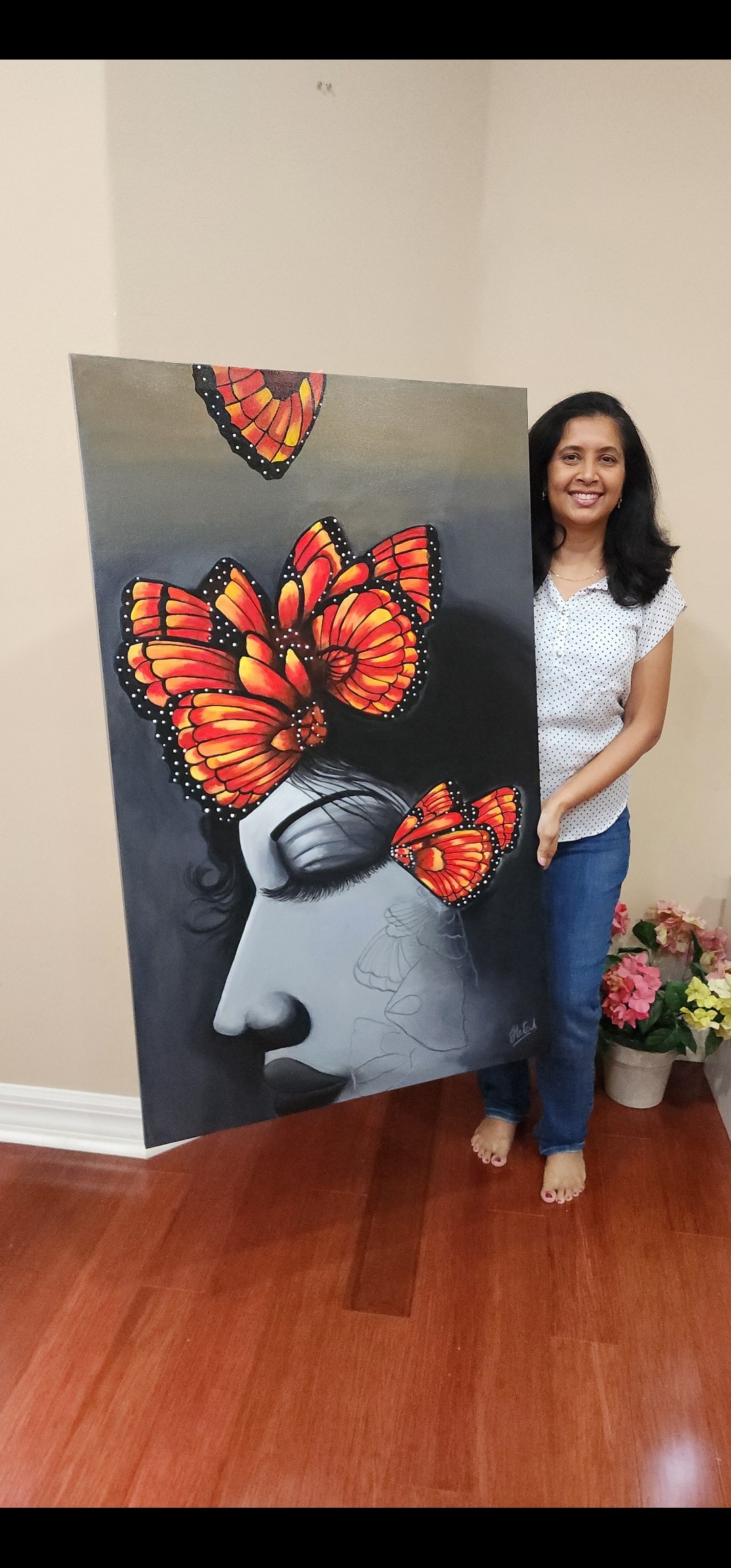 Woman standing next to a large butterfly-themed artwork on a wall, with flowers on the floor nearby.