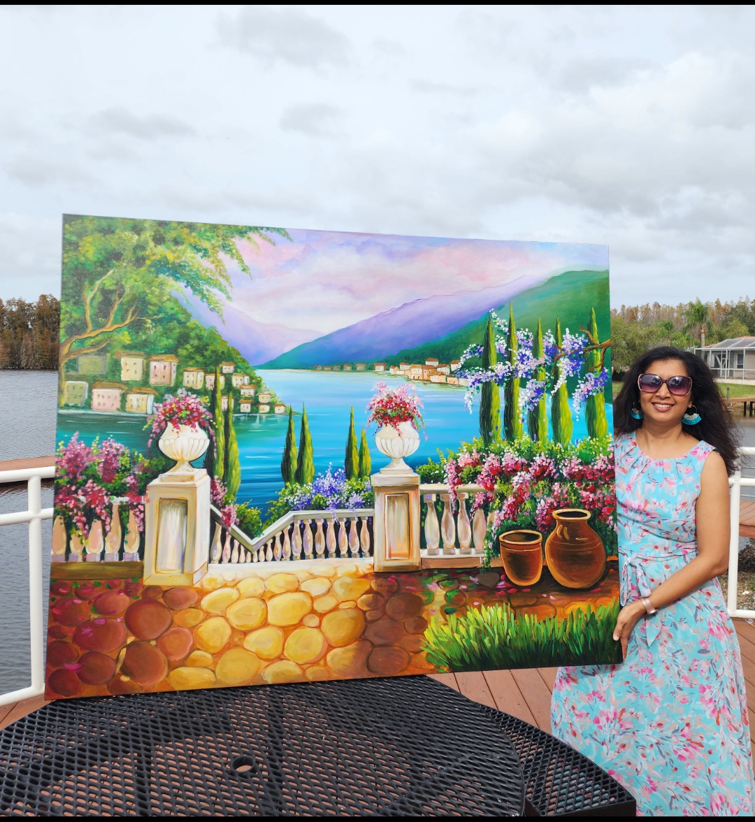 Woman in a floral dress standing next to a colorful landscape painting outdoors, cloudy sky above.