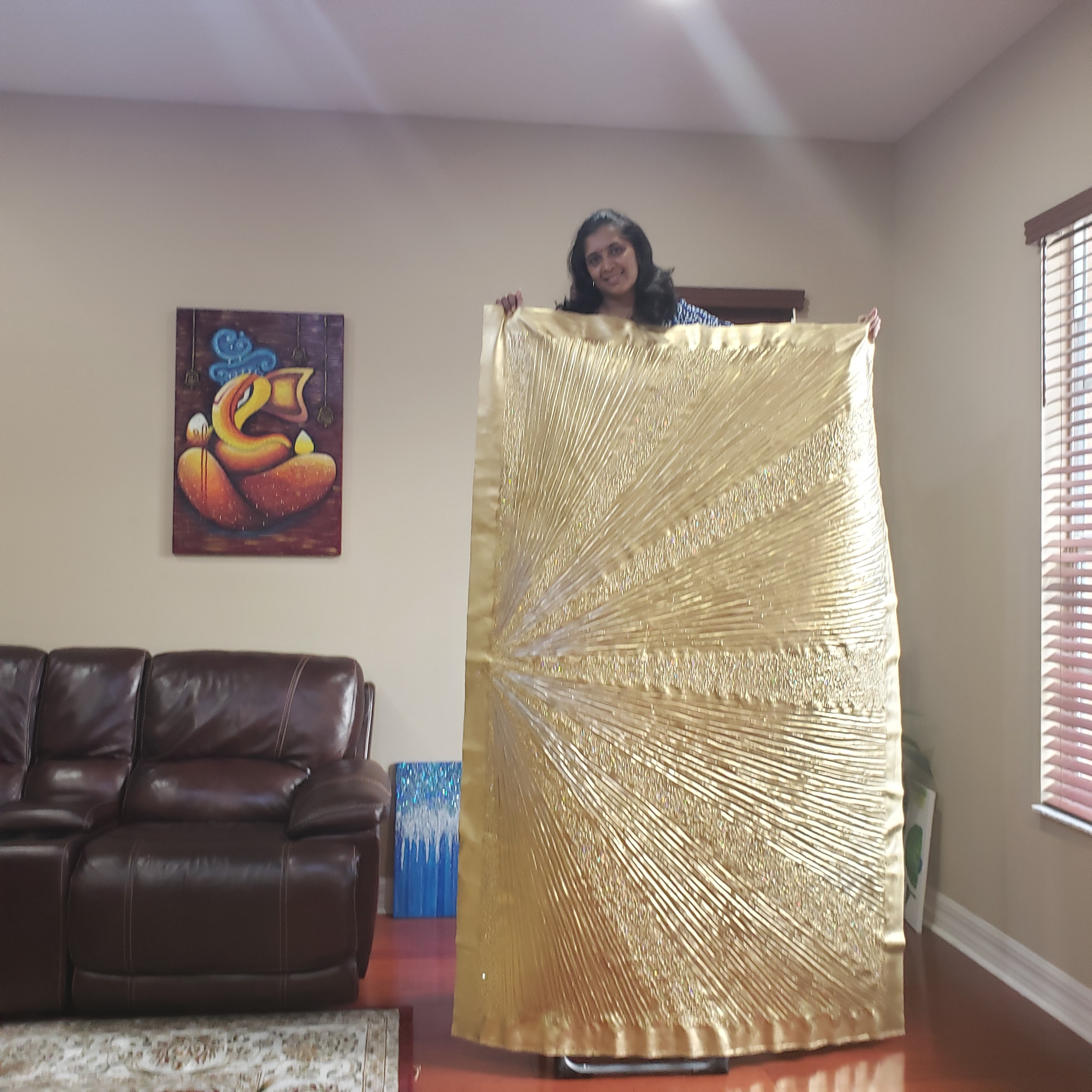 Woman holding a large gold fabric in a living room with a brown sofa and artwork on the wall.