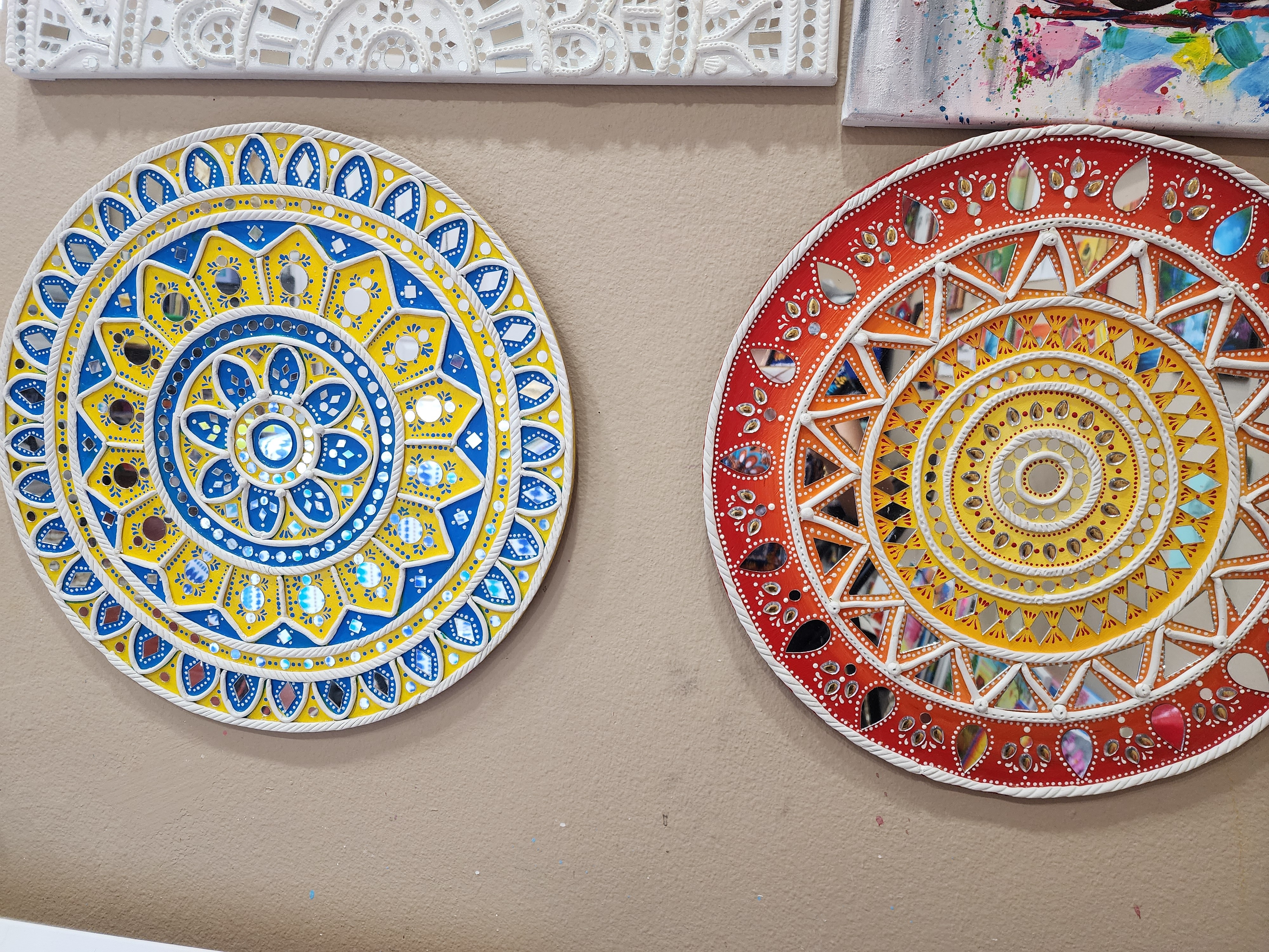 Two decorative plates with intricate patterns, one with blue and yellow colors, the other with red and yellow, on a beige surface.