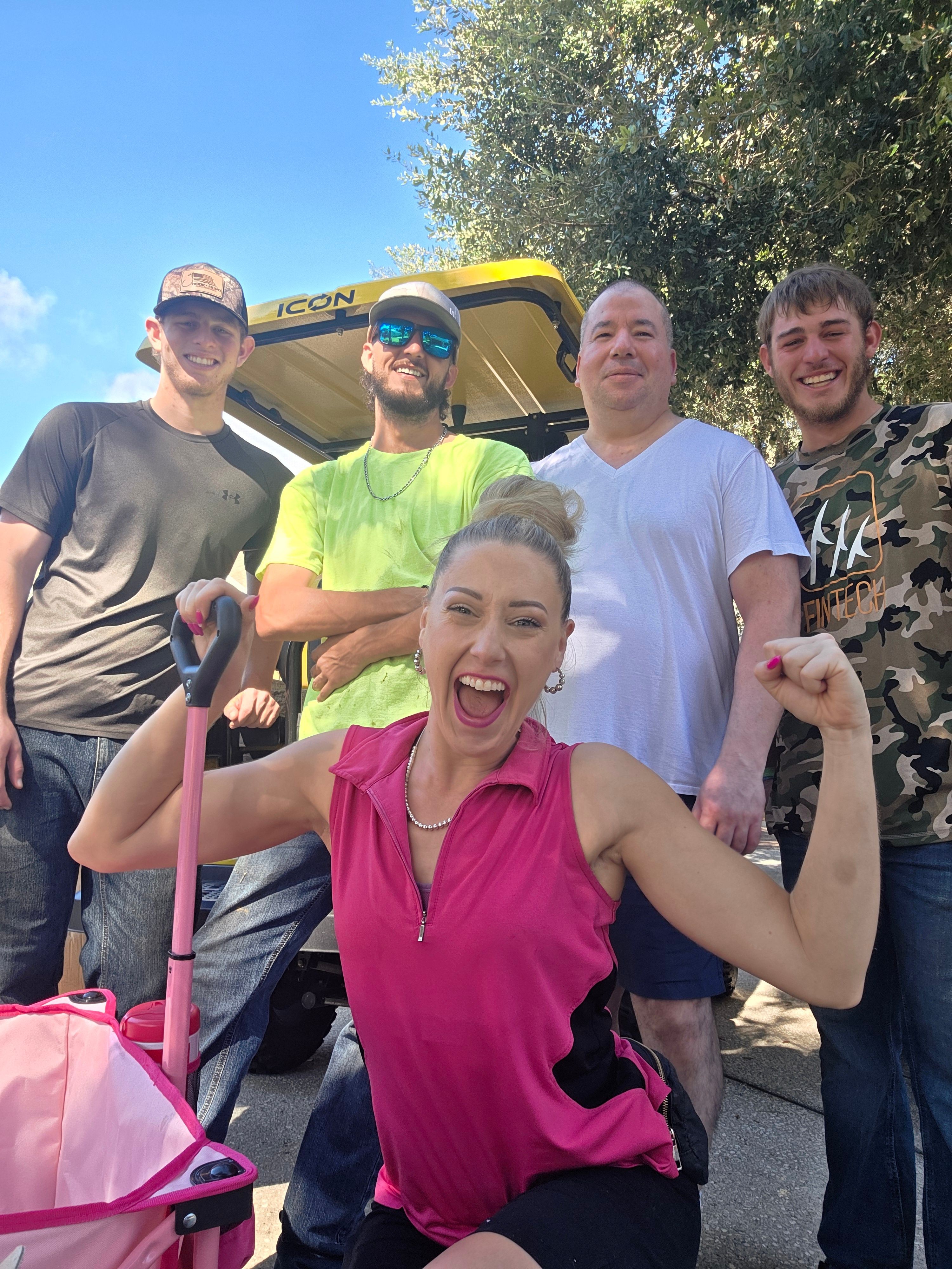 Group of people outdoors, smiling and posing for a photo, with trees and a blue sky in the background.