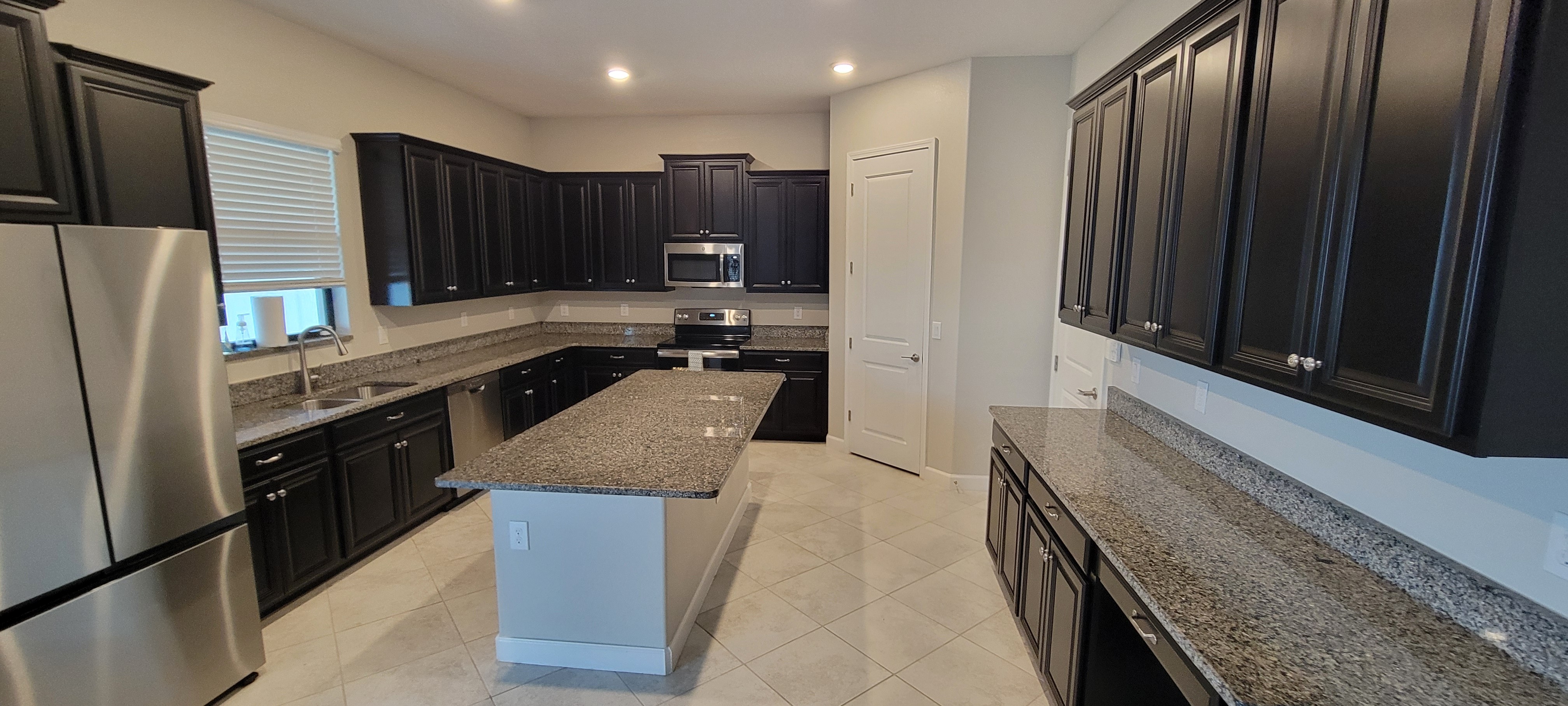 Modern kitchen with dark cabinets, granite countertops, stainless steel appliances, and a central island, well-lit with ceiling lights.