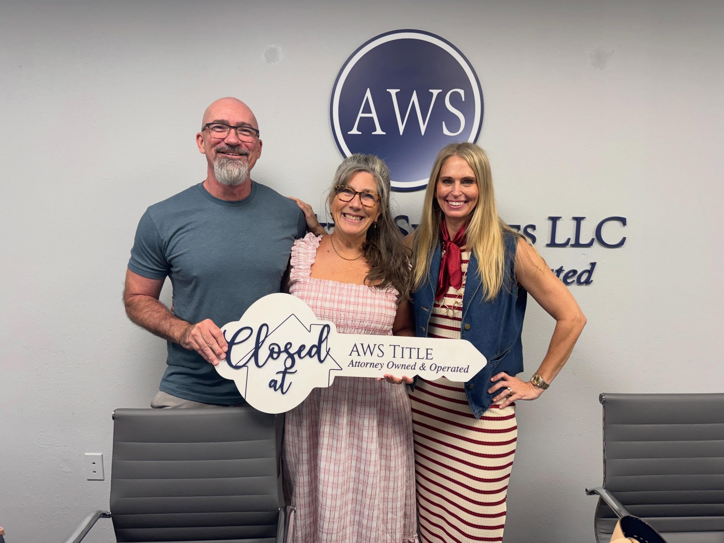 Three people standing in front of a wall with AWS logo, holding a sign that says 'Closed at AWS TITLE'.