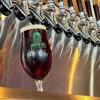 A glass of dark beer with a green logo, placed under beer taps, on a bar counter.