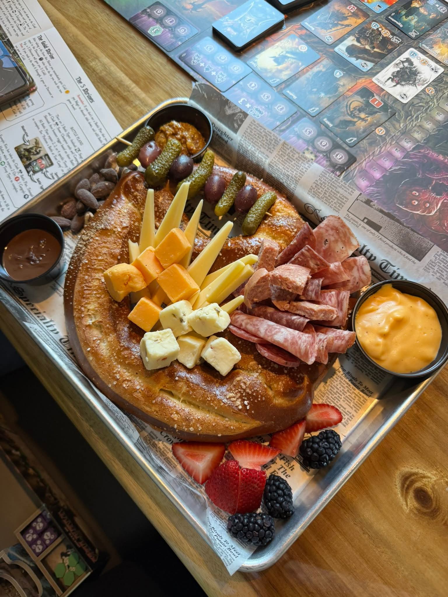 Tray with cheese, meats, strawberries, blackberries, and a small bowl of orange sauce on a wooden table.