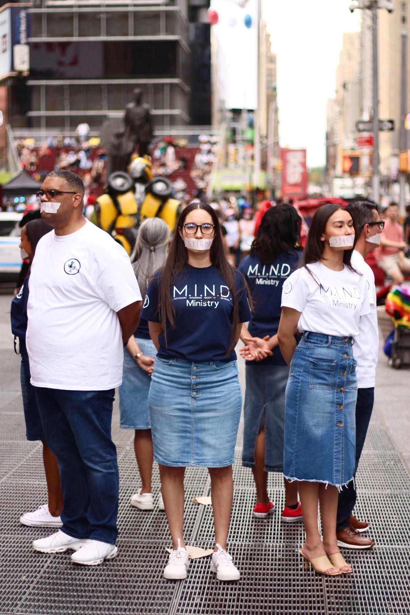 Group of people walking on city street, wearing masks, with buildings and vehicles in background.
