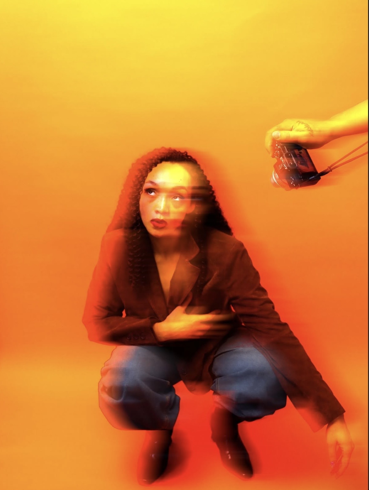Person crouching with blurred motion, holding a glass, against a yellow-orange background.