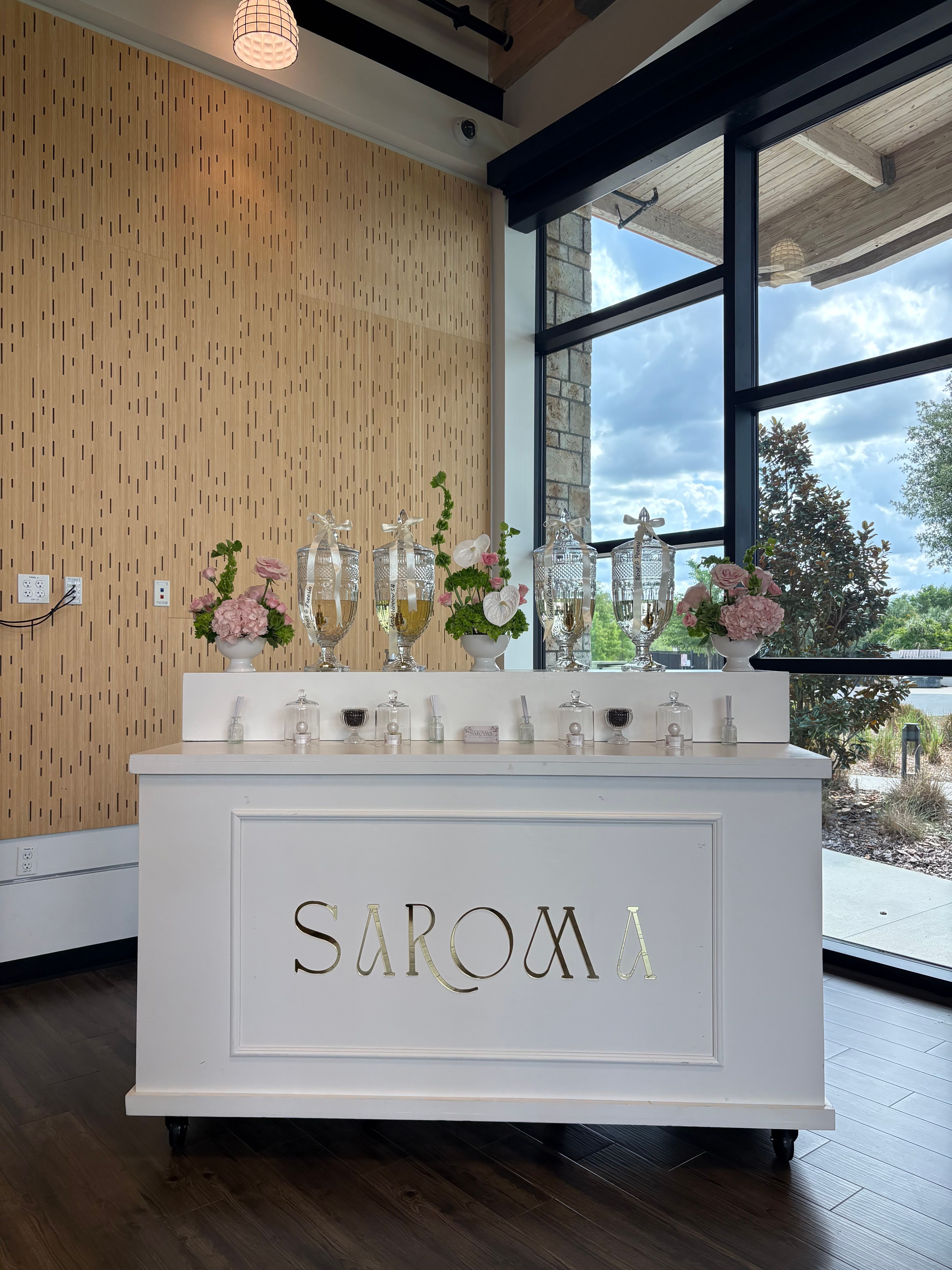 White table with flowers and candles, sign reads 'SADOMI', in a room with large windows and wooden floor.