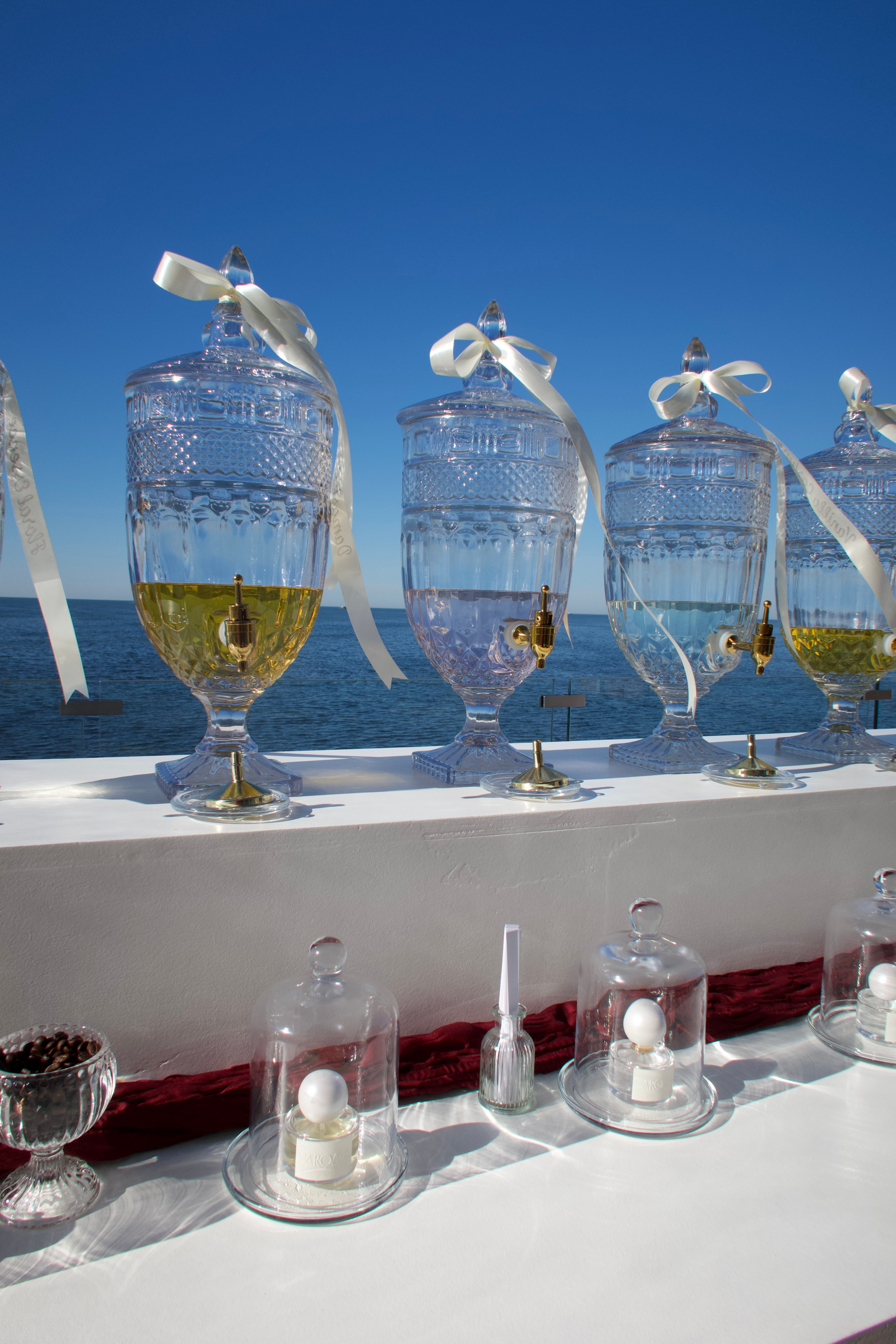 Four glass jars with ribbons and yellow liquid, lined up on a white surface against a blue sky background.
